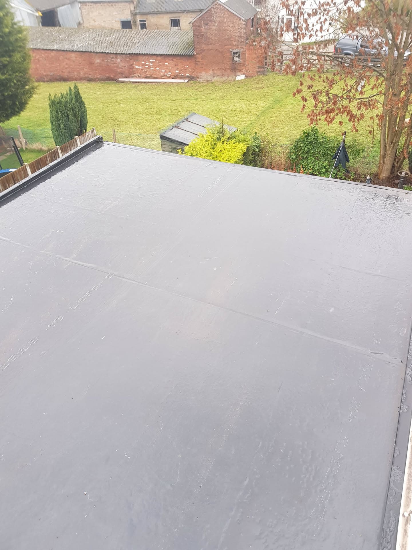 Completed grey EPDM rubber flat roof extension overlooking residential garden