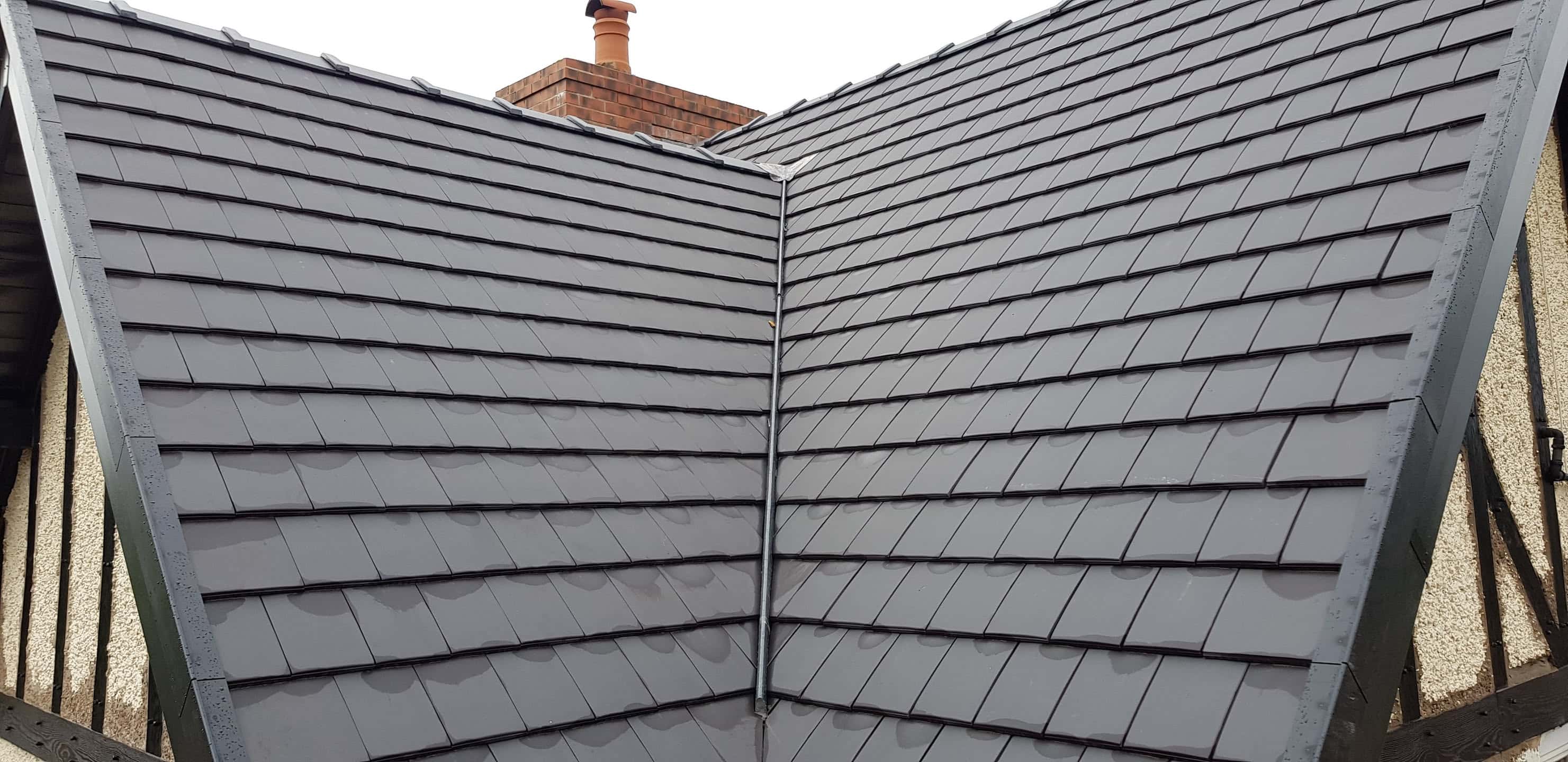 Newly completed pitched roof with grey slate tiles and ridge detail, chimney visible in background