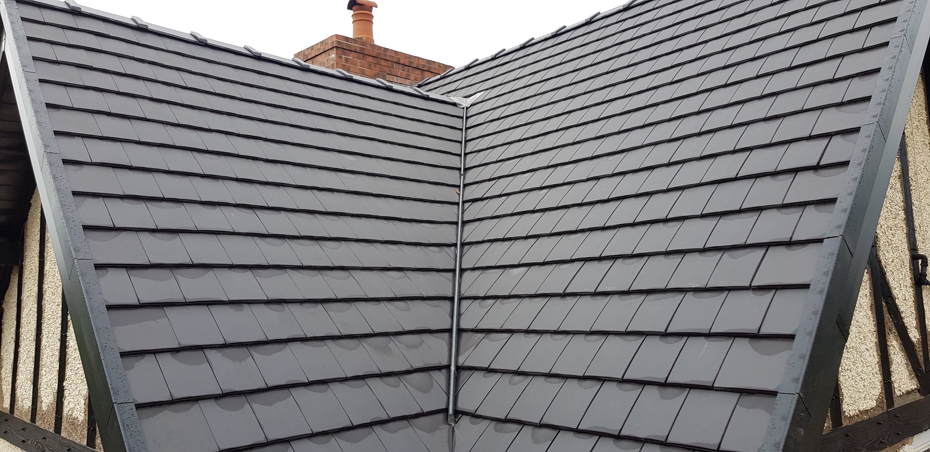 Newly completed pitched roof with grey slate tiles and ridge detail, chimney visible in background