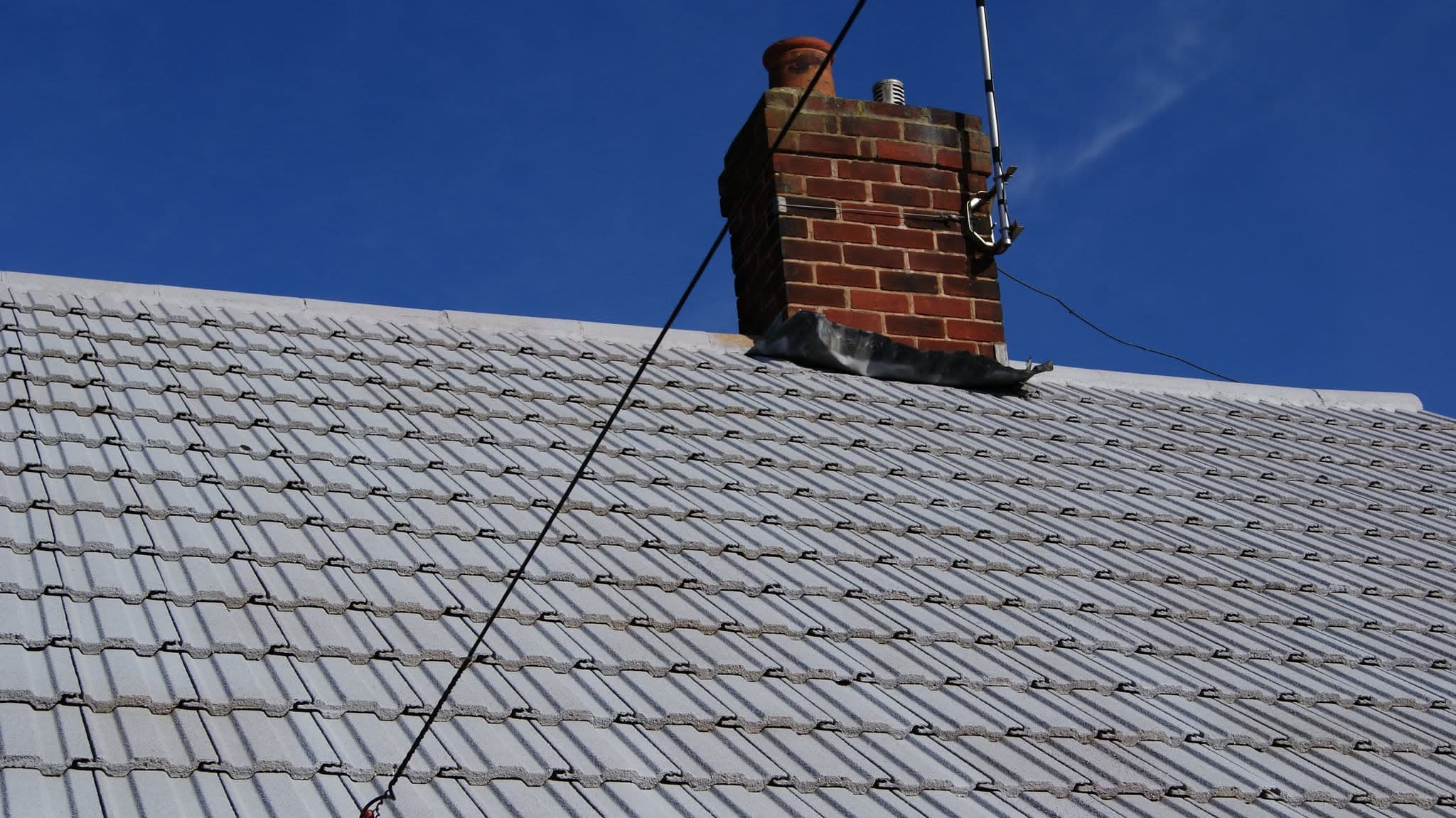 Grey concrete tiled pitched roof with brick chimney stack and terracotta pot