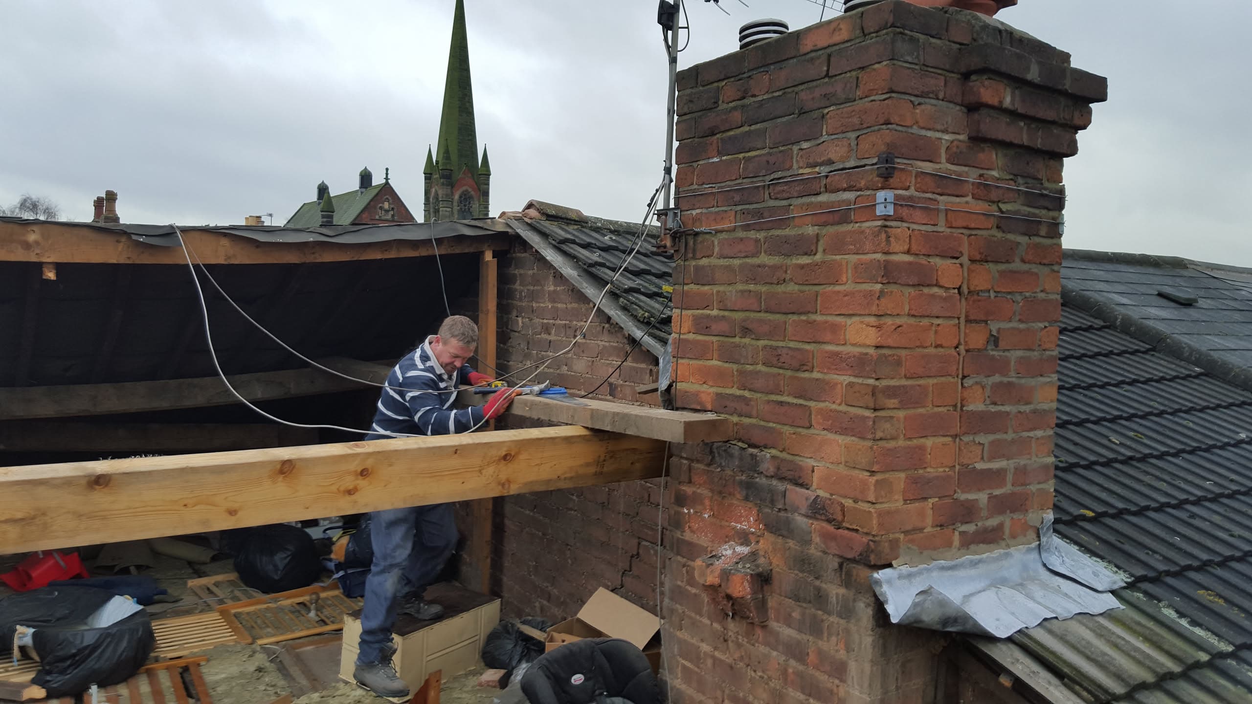 Roofer working on chimney stack with exposed timber framework on pitched slate roof