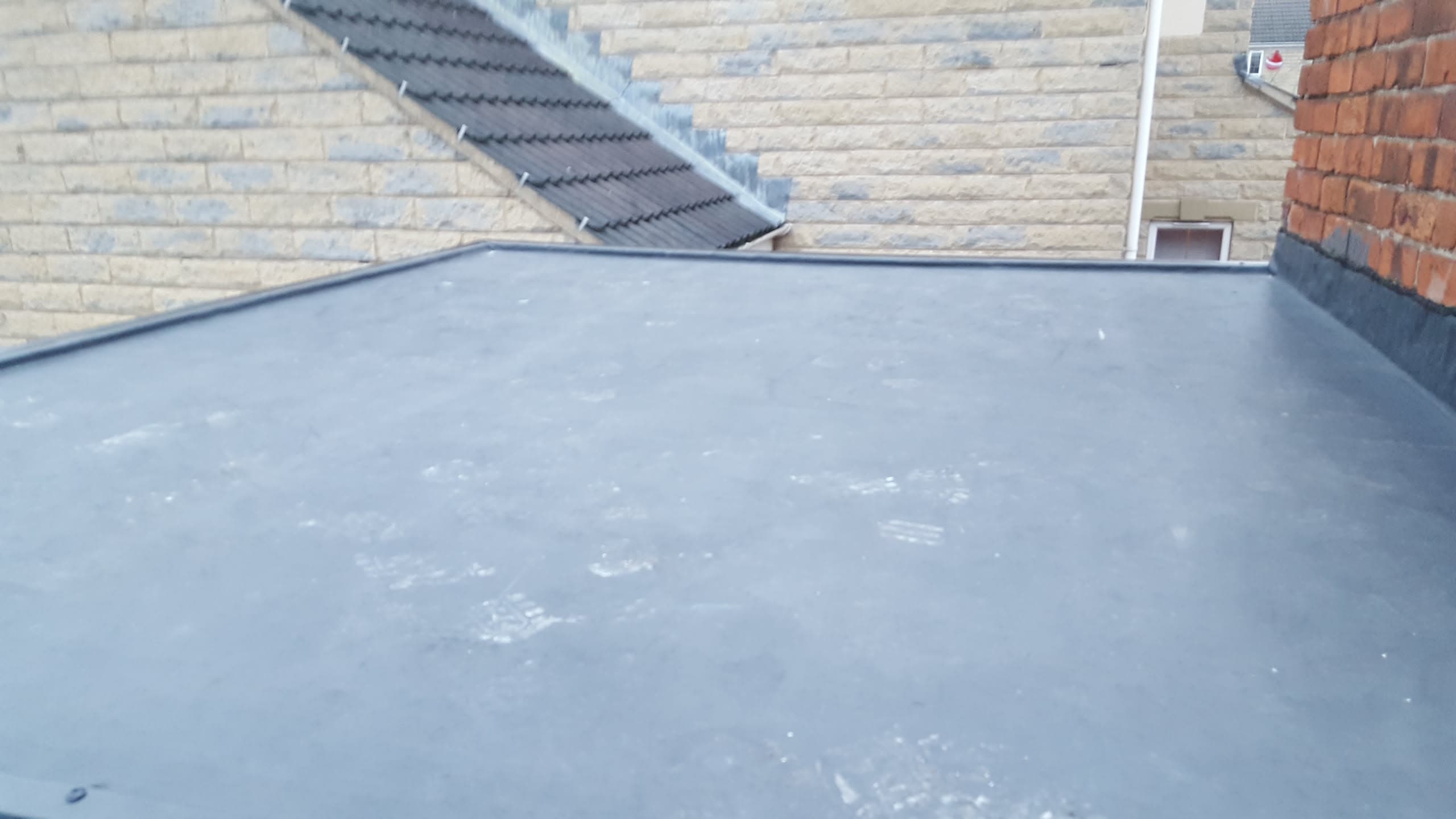 Grey flat roof with GRP fibreglass finish between brick walls and tiled pitched roofs