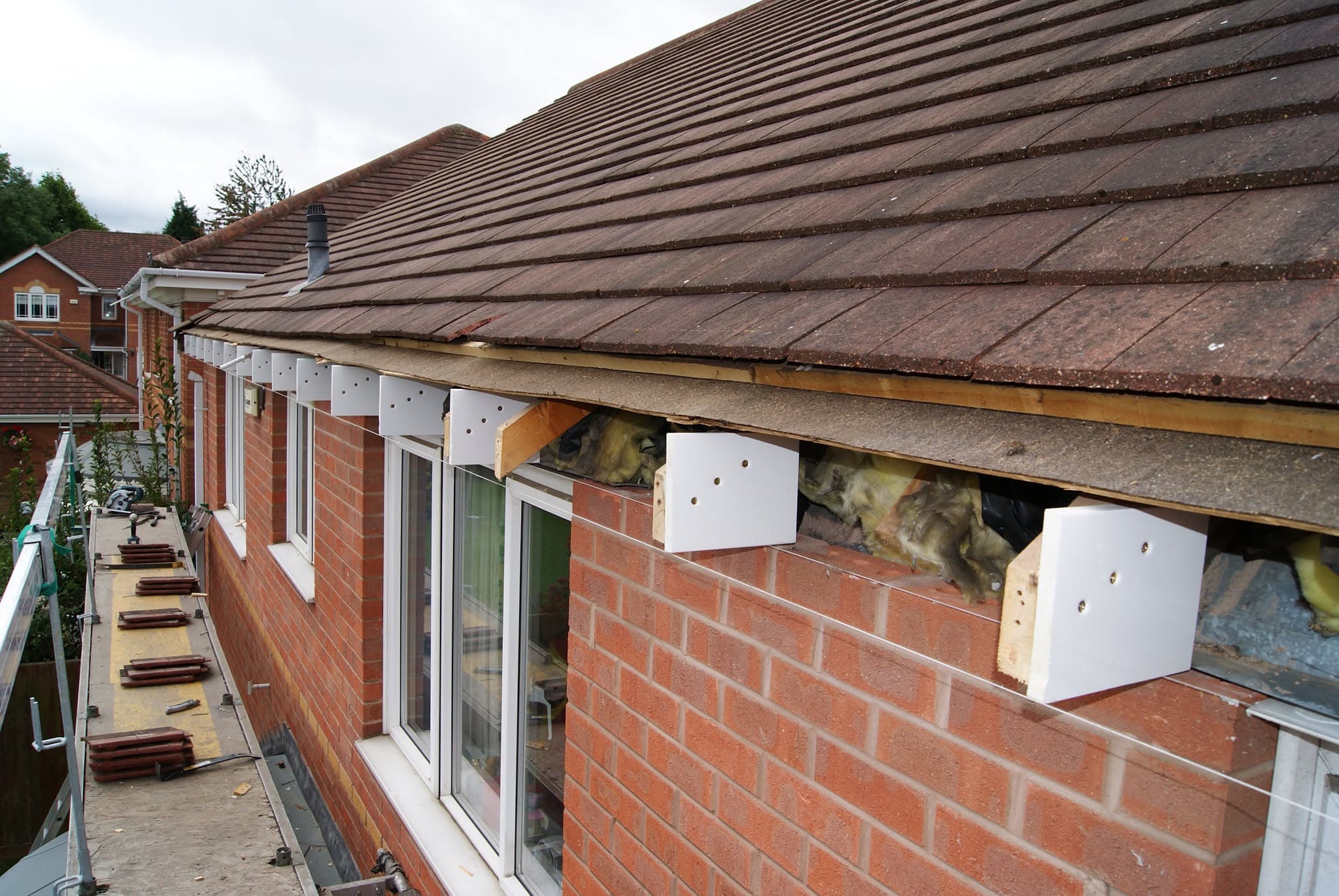 Pitched roof with brown concrete tiles and exposed fascia boards during installation on brick property