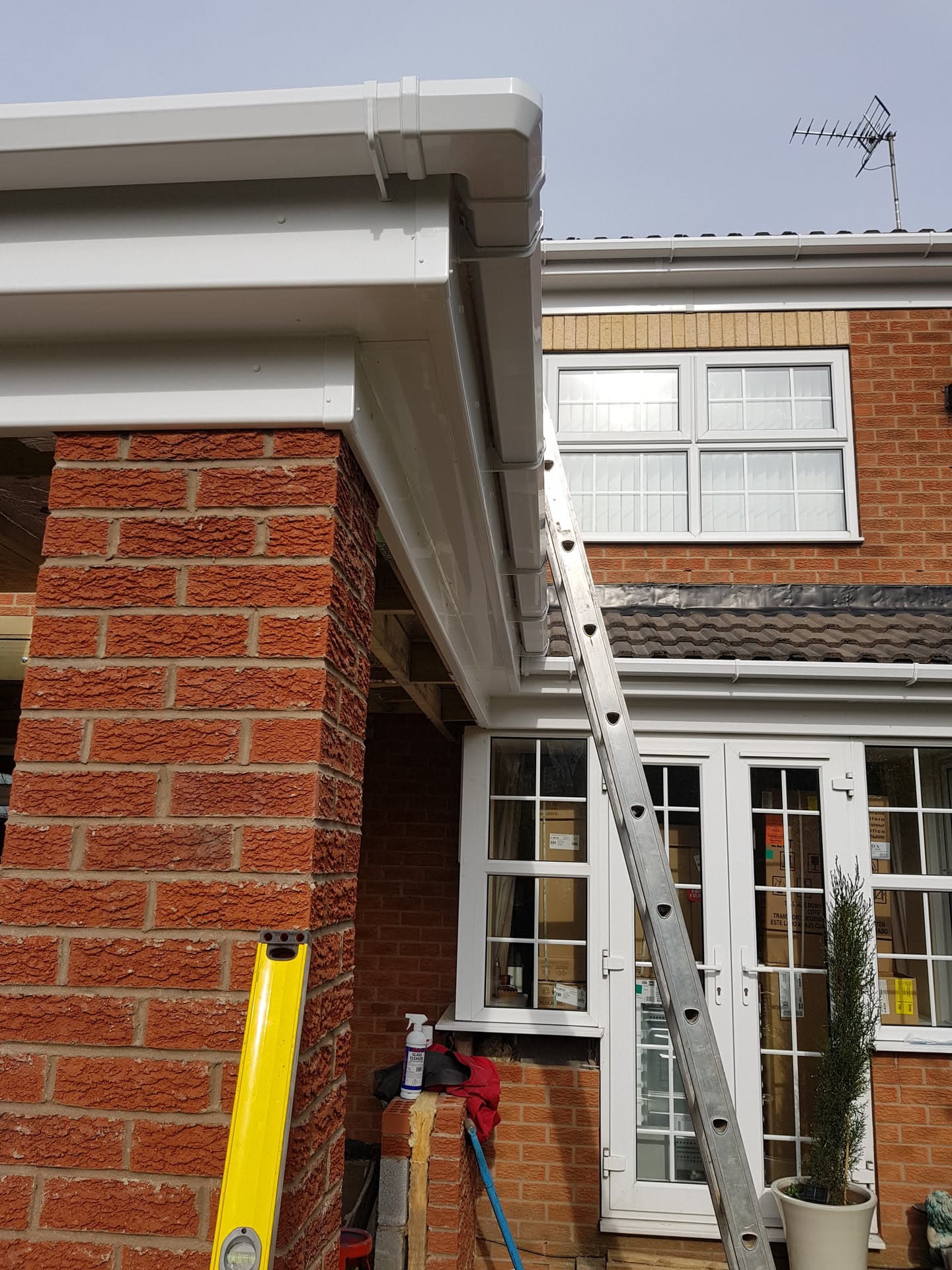 White fascias, soffits and brown guttering installed on red brick house with ladder against wall