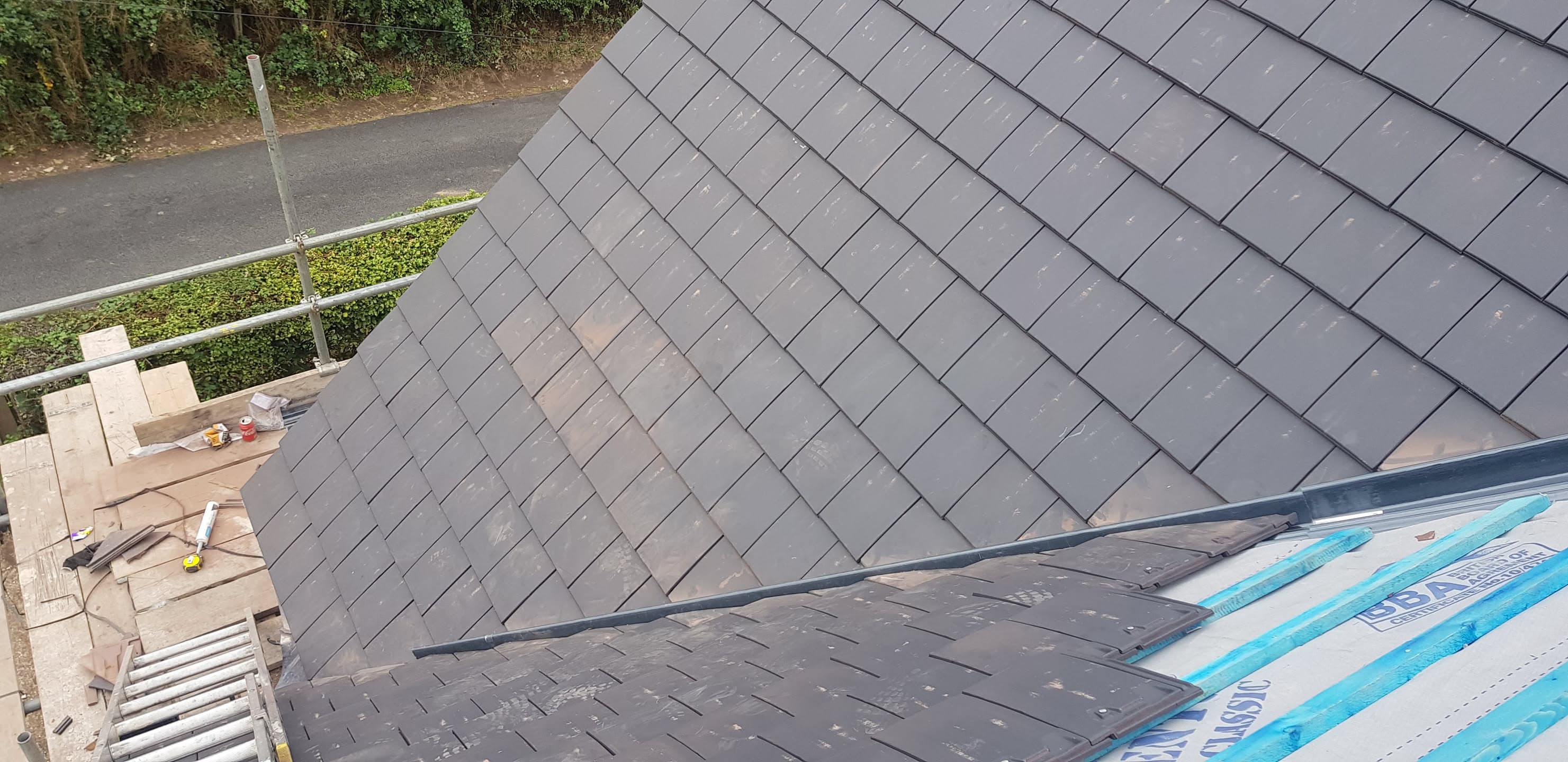Grey slate pitched roof with scaffolding and roofing materials visible on platform
