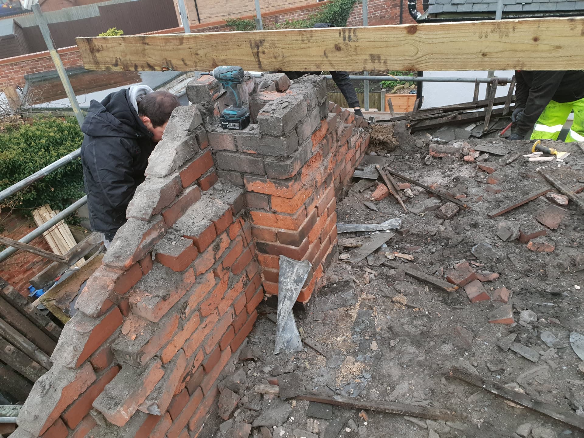 Fitters rebuilding brick chimney stack on flat roof with debris from demolition