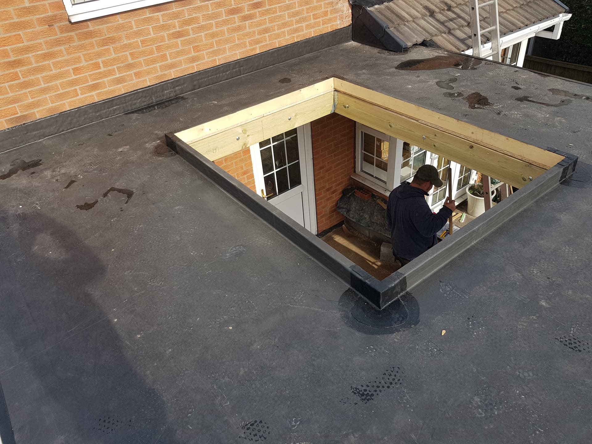 Fitter installing timber frame for flat roof skylight on grey felt roof