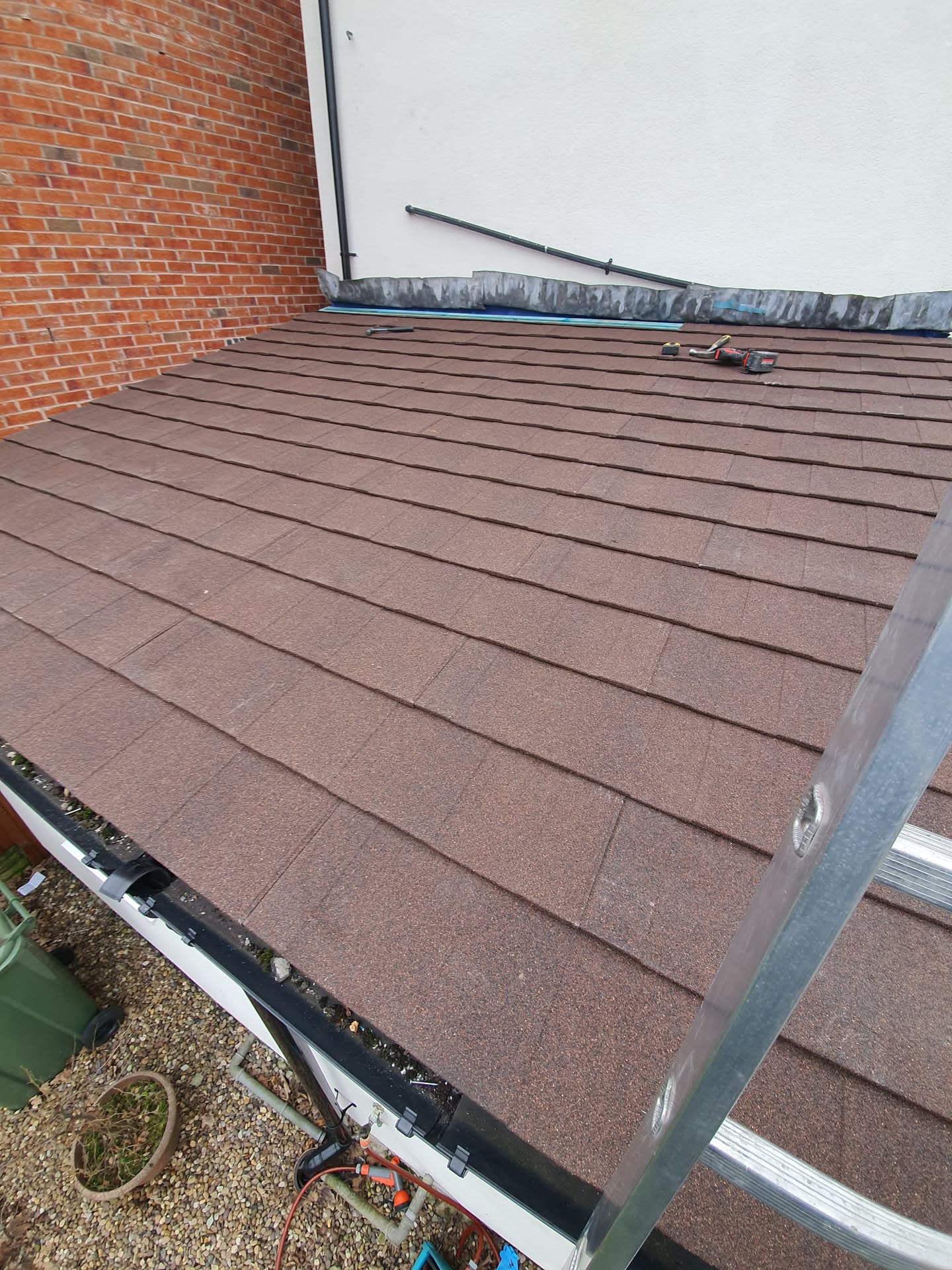 Pitched roof with brown concrete tiles and black guttering against brick wall