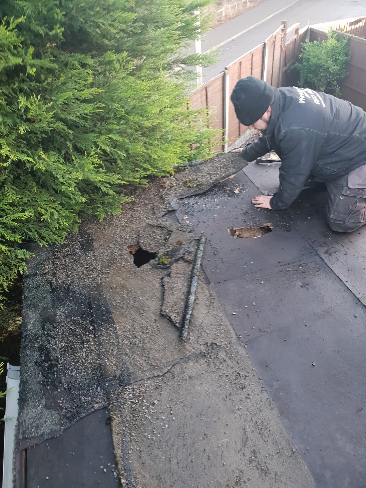 Roofer installing felt on flat roof with visible old and new roofing material
