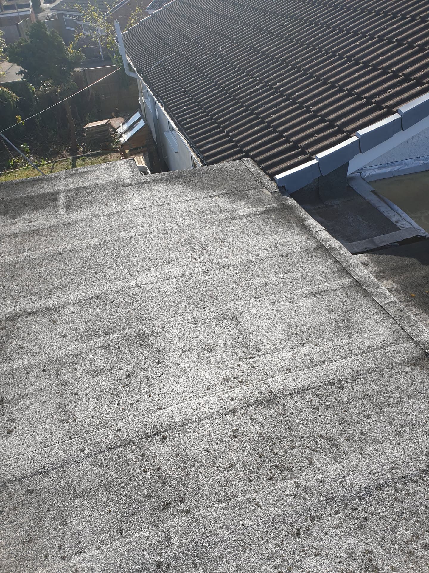 Flat roof with grey felt surface and white guttering on pitched tiled roof