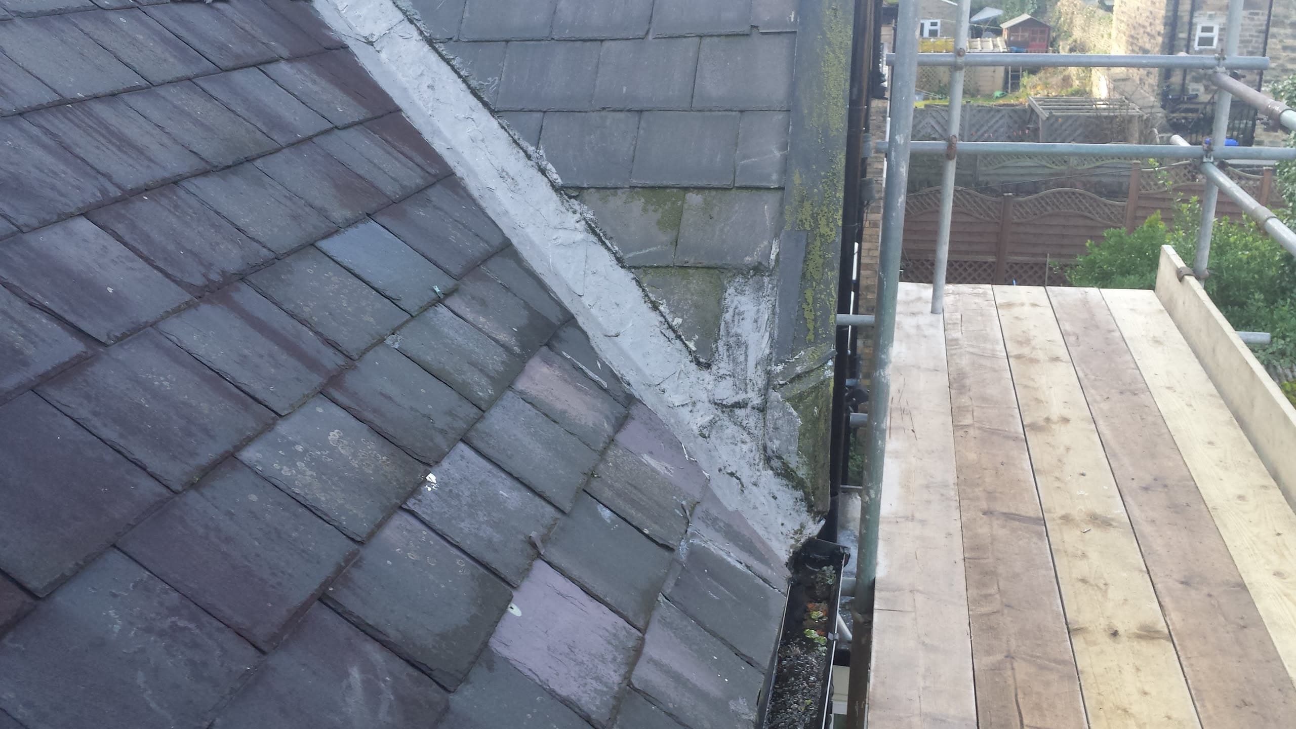 Grey slate pitched roof with scaffolding platform alongside ridge and chimney stack