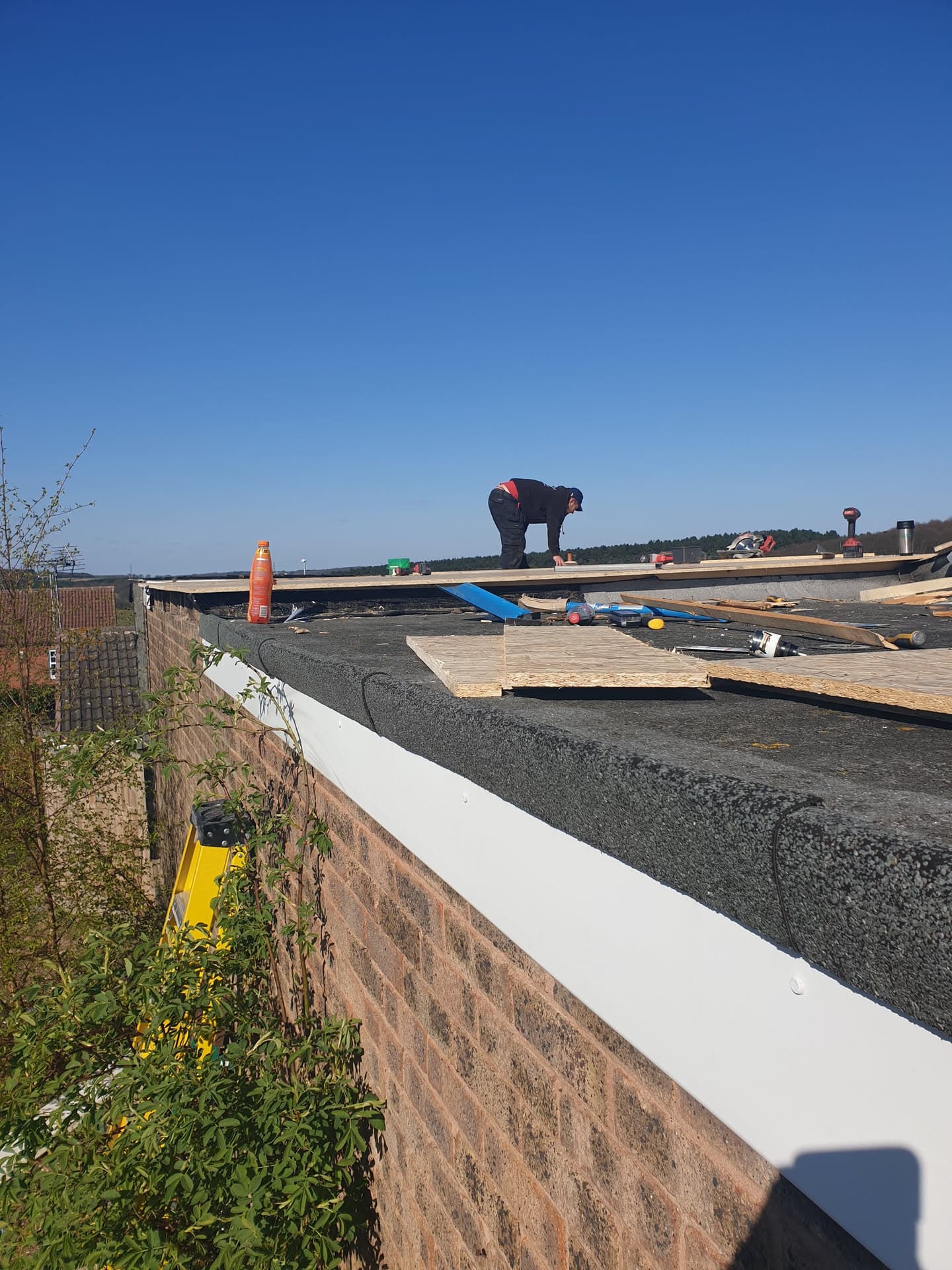 Fitter working on flat roof installation with timber decking and felt underlay