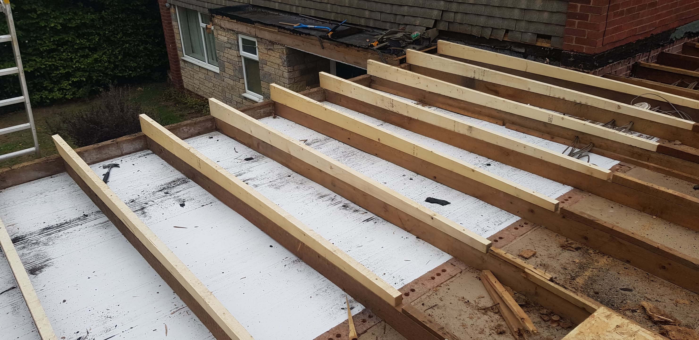 Flat roof construction with new timber joists and white membrane underlay in progress