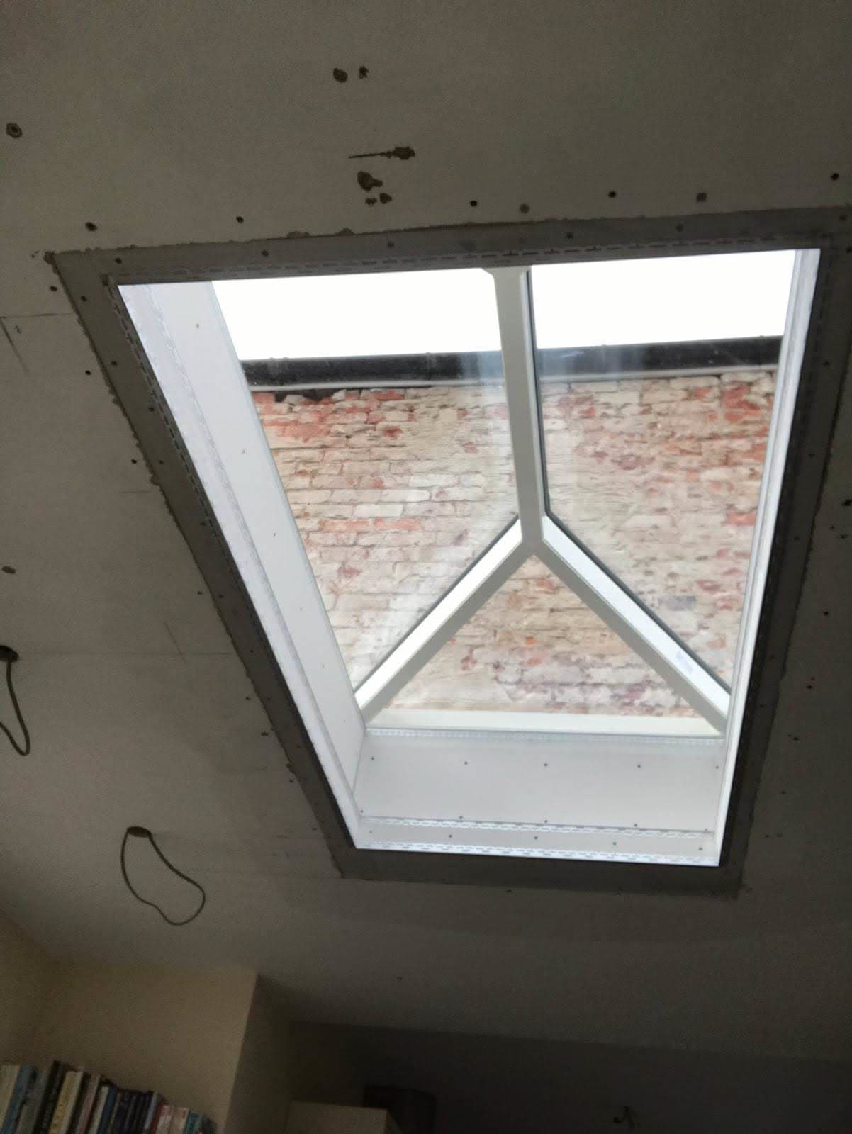White-framed roof window installed in plasterboard ceiling with brick chimney visible outside