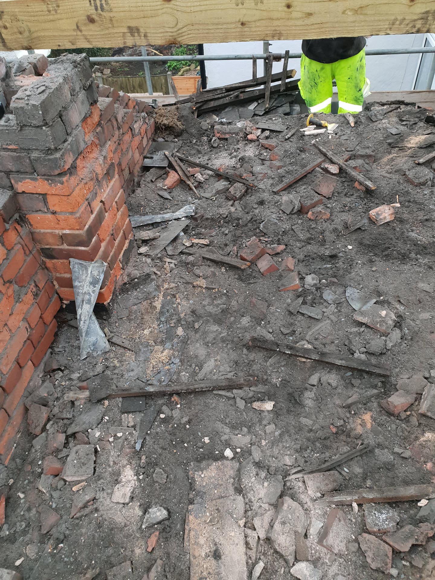 Flat roof demolition in progress with exposed brick chimney and fitter in high-visibility jacket