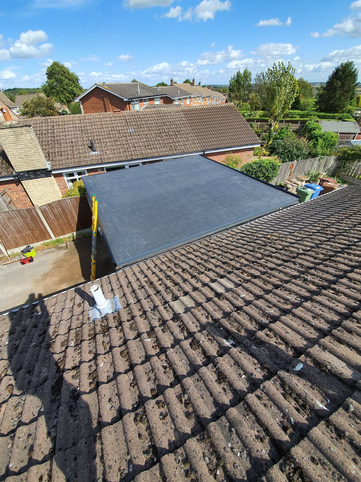 Pitched roof with brown concrete tiles and new flat roof extension with dark grey felt covering