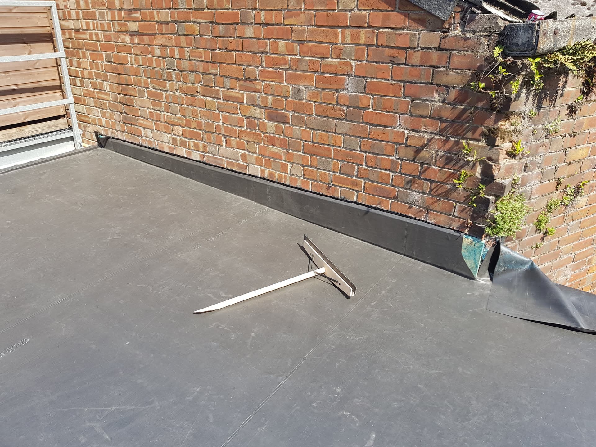 Grey EPDM rubber flat roof with upstand against brick wall