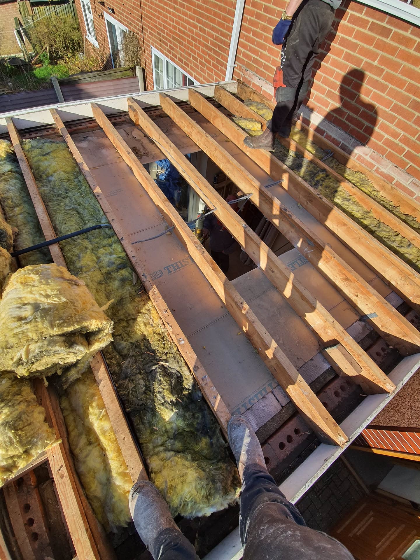 Flat roof replacement in progress with exposed timber joists and insulation, fitter working on brick building