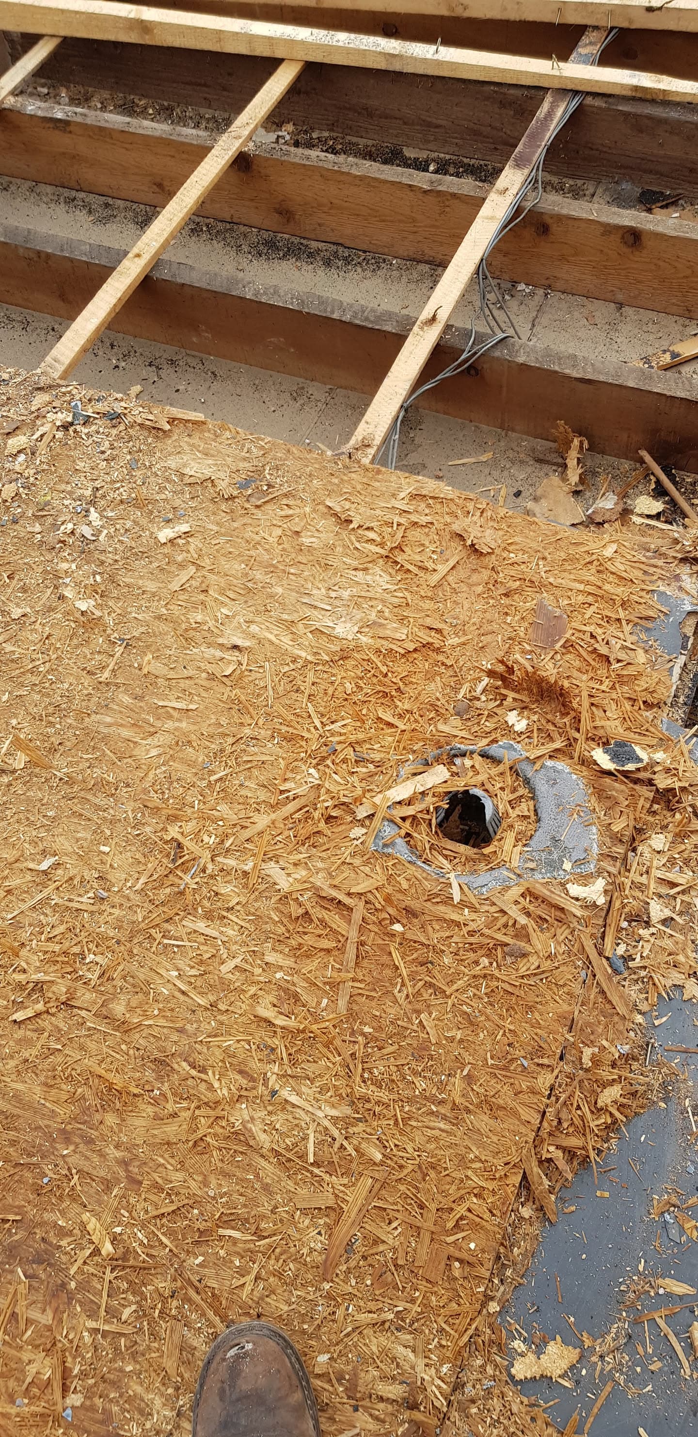 Exposed flat roof decking with damaged chipboard and visible roof joists during repair work