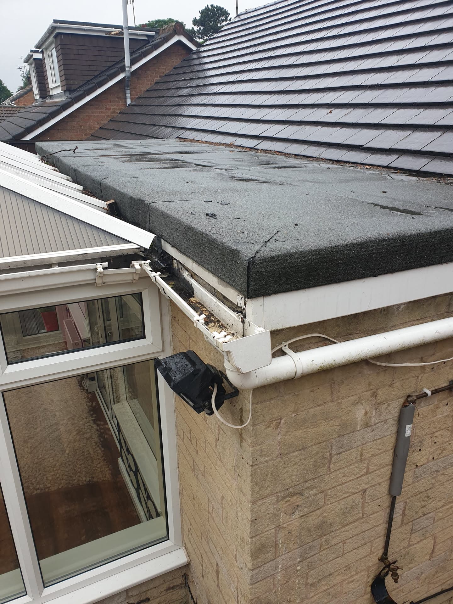 Flat roof with grey felt covering and white fascias and guttering on residential property