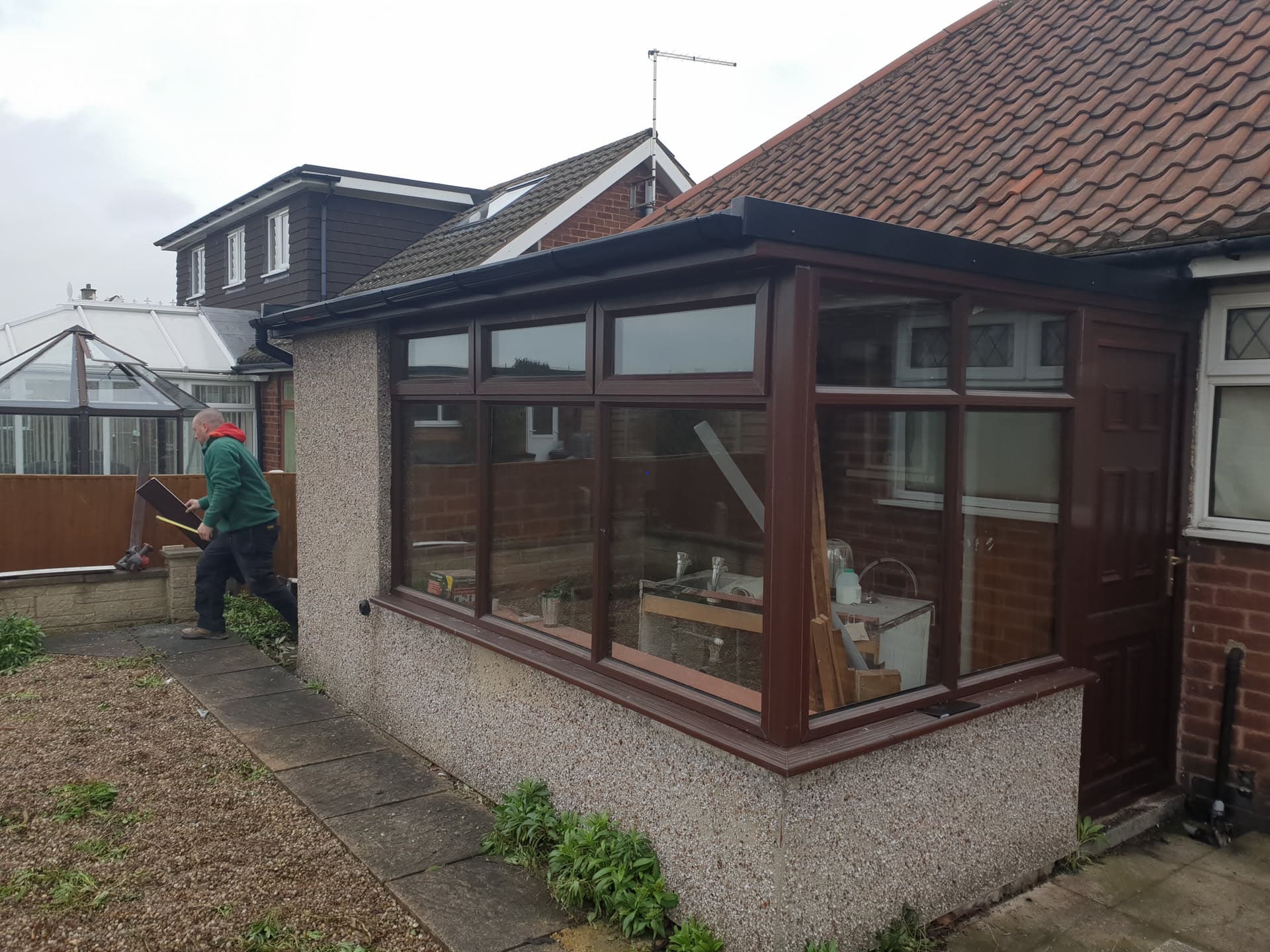 Conservatory with dark flat roof and brown uPVC frames attached to brick house