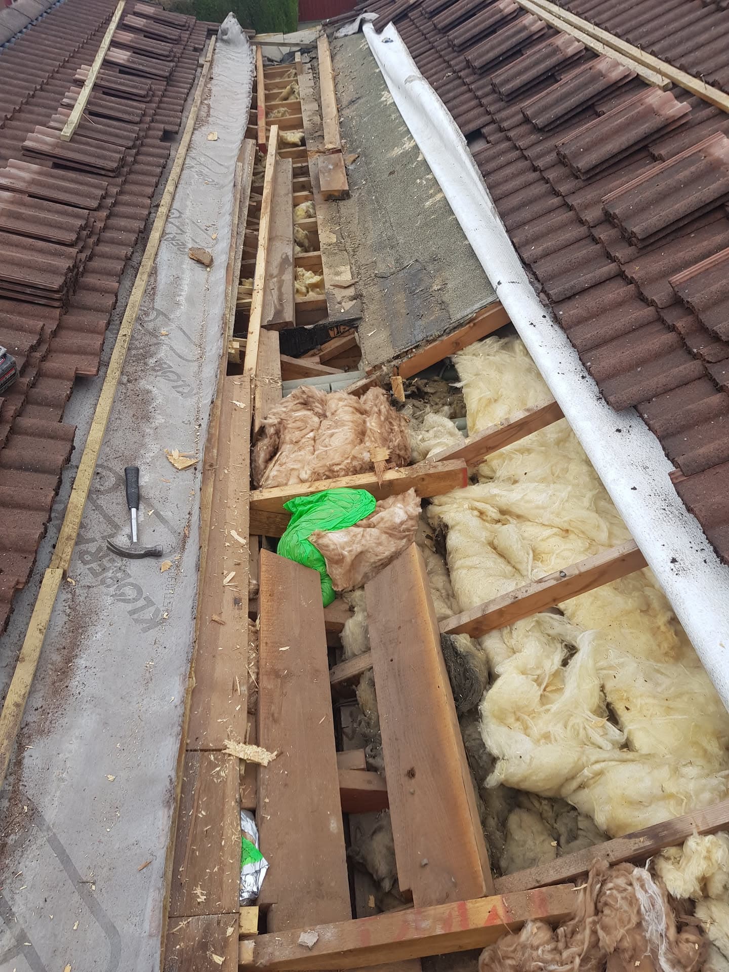 Pitched roof with brown concrete tiles partially removed, exposing timber joists and insulation during repair work