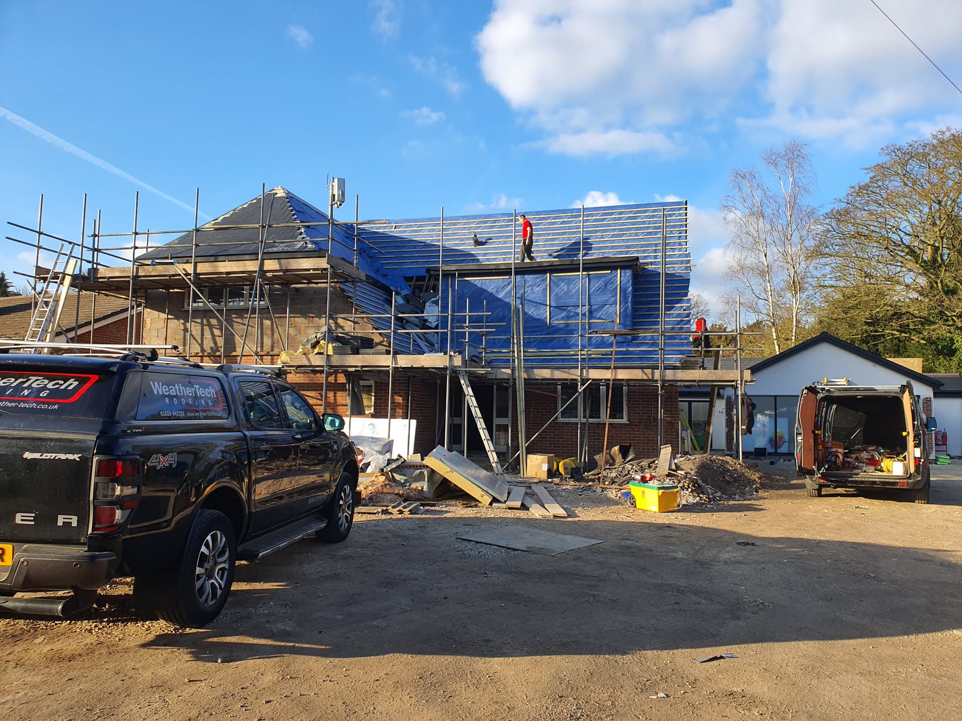 New build property with pitched roof covered in blue protective sheeting and scaffolding