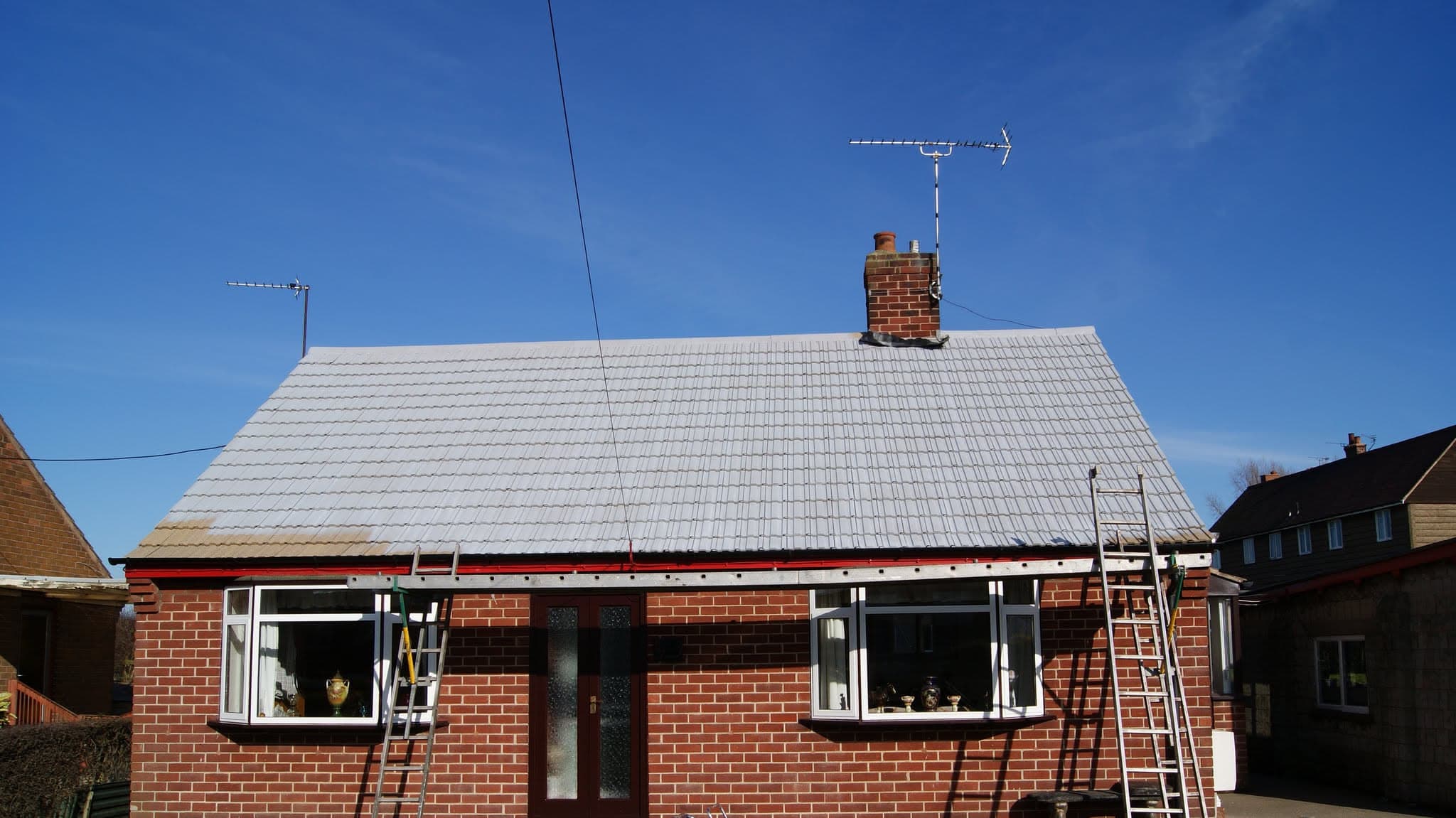 Pitched roof with light grey concrete tiles and brick chimney stack with TV aerial