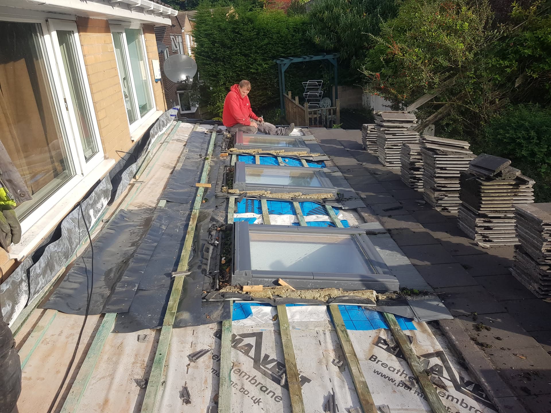 Fitter installing slate tiles on flat roof with skylights and stacked materials