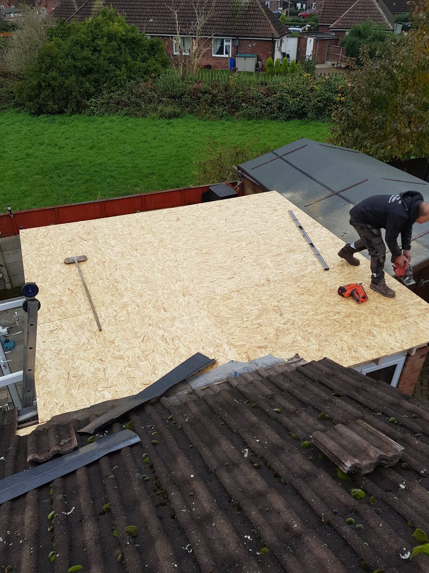 Fitter installing new OSB decking on flat roof extension with old concrete tiled roof in foreground
