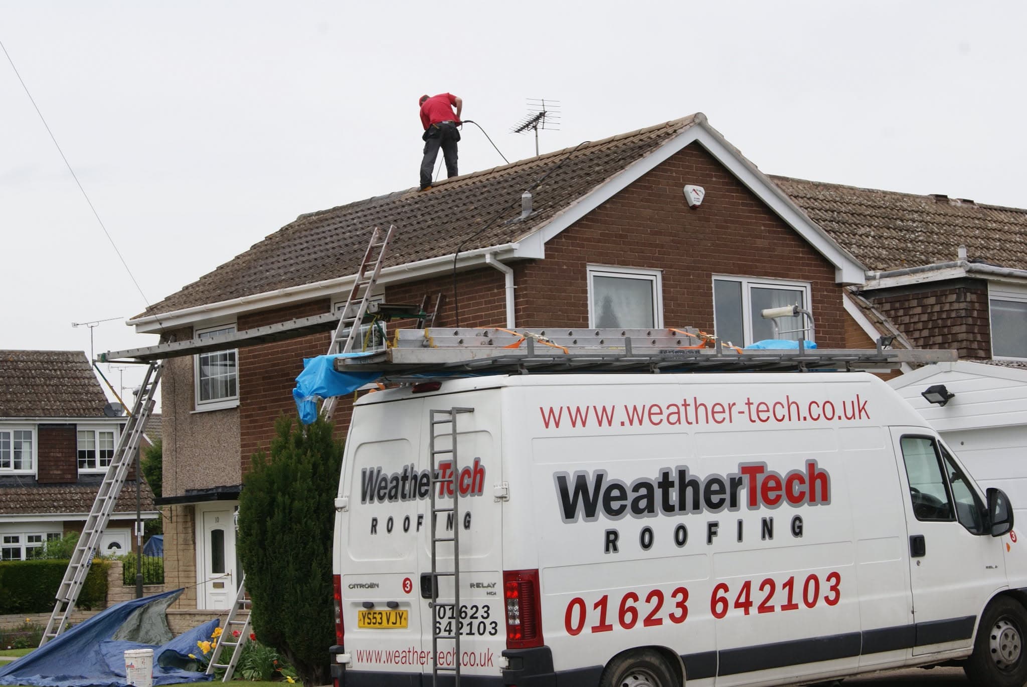 Fitter working on brown tiled pitched roof with WeatherTech van parked below
