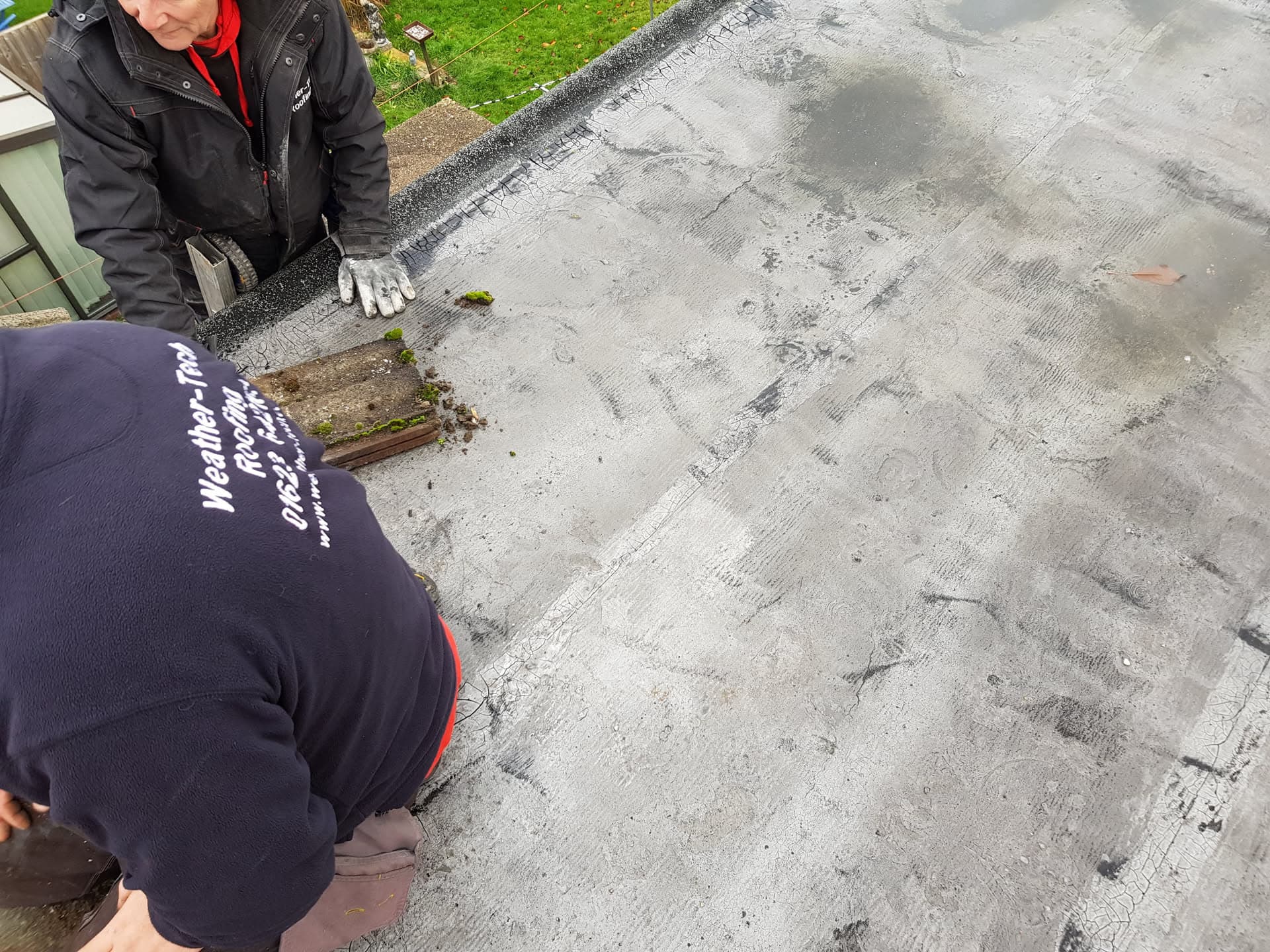 WeatherTech fitters inspecting grey felt flat roof surface with visible wear