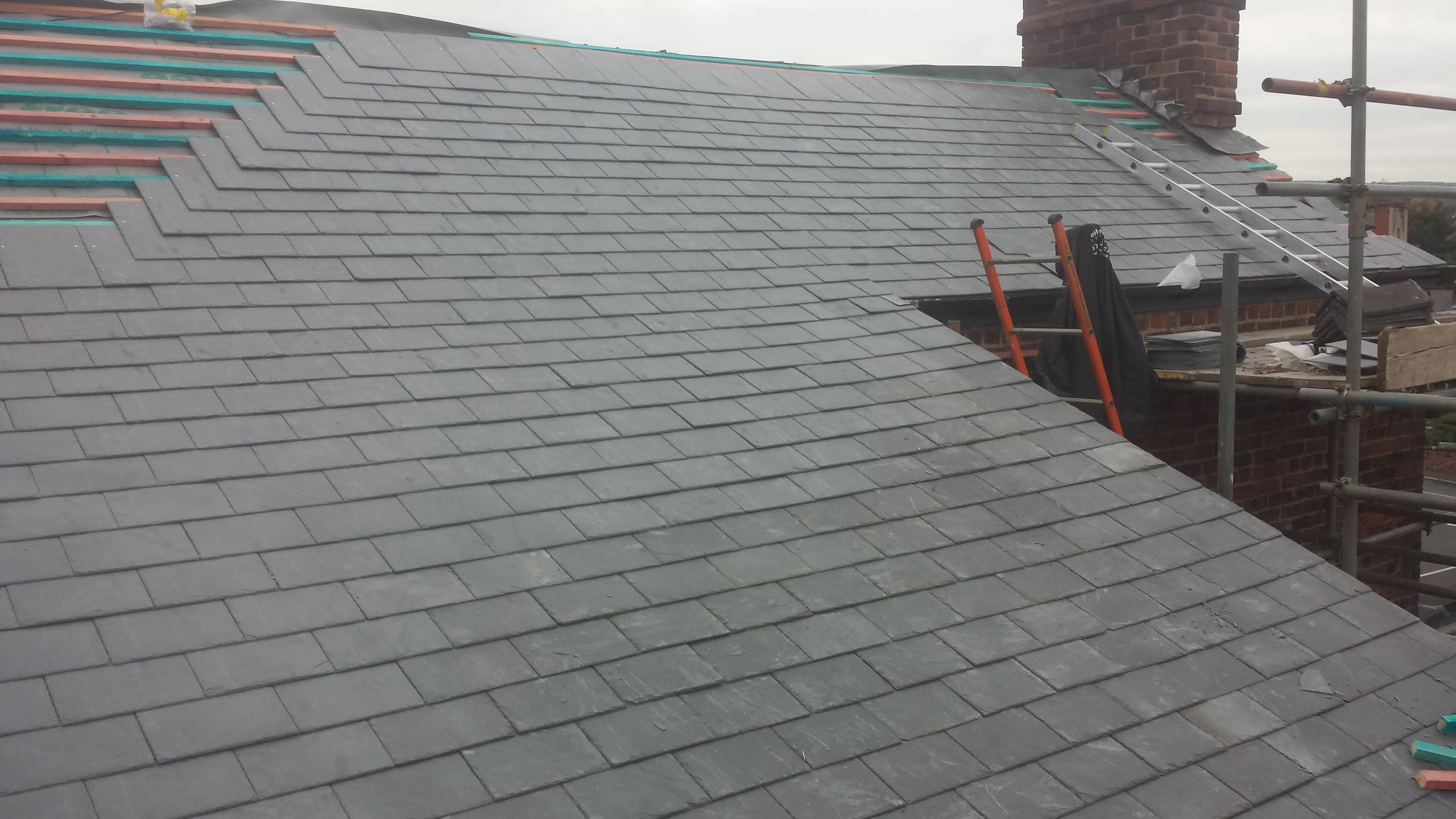 Grey slate pitched roof with ridge tiles, chimney stack and scaffolding