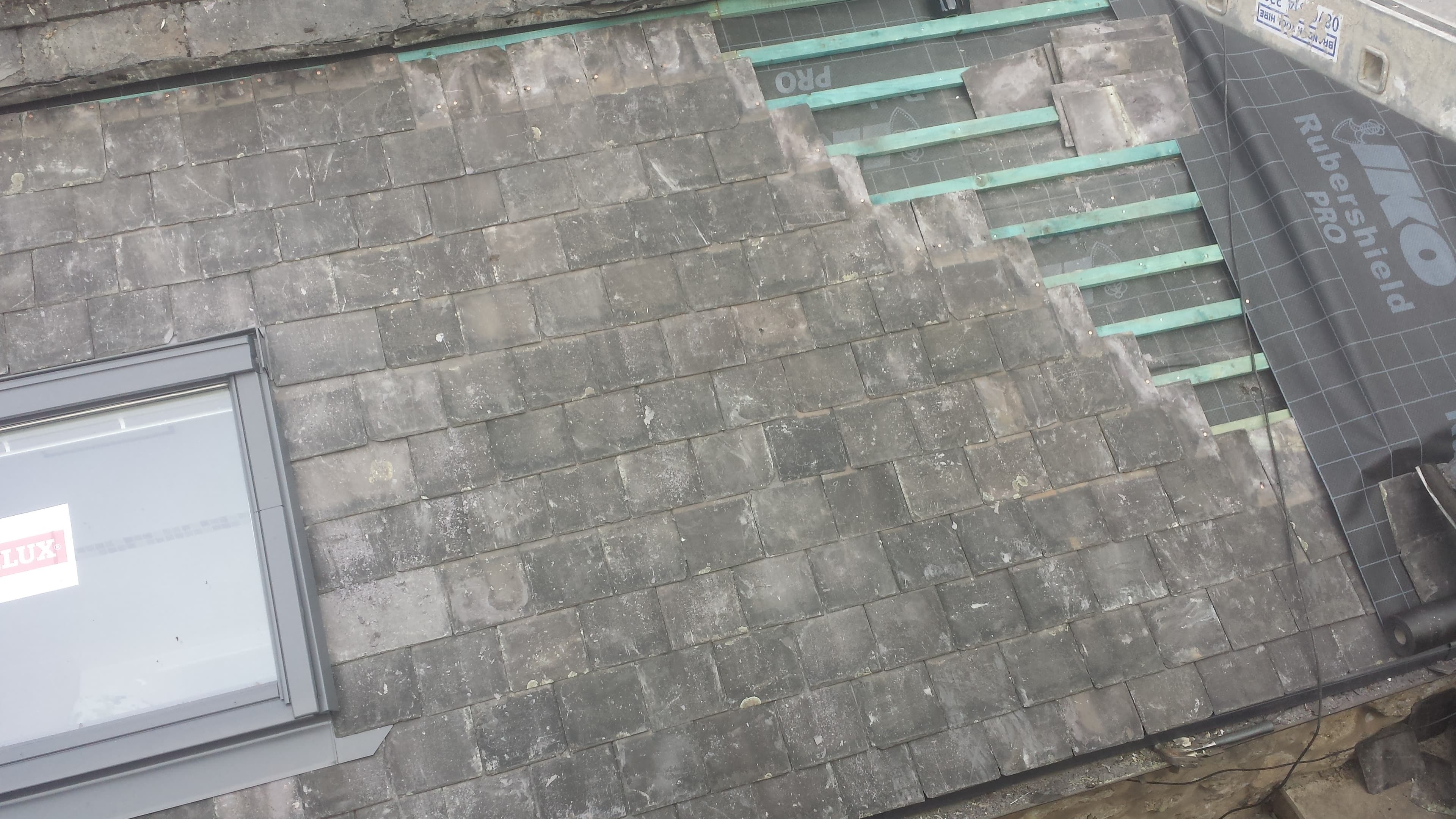 Aerial view of weathered grey slate pitched roof with green battens visible during repair work