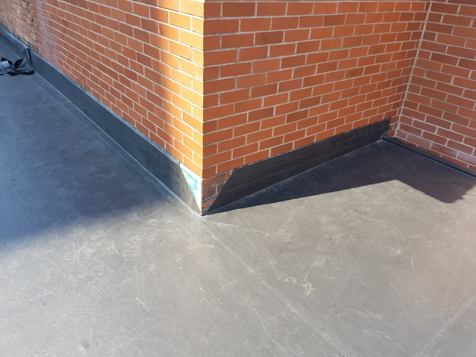 Flat roof with grey GRP fibreglass finish and black lead flashing around brick chimney