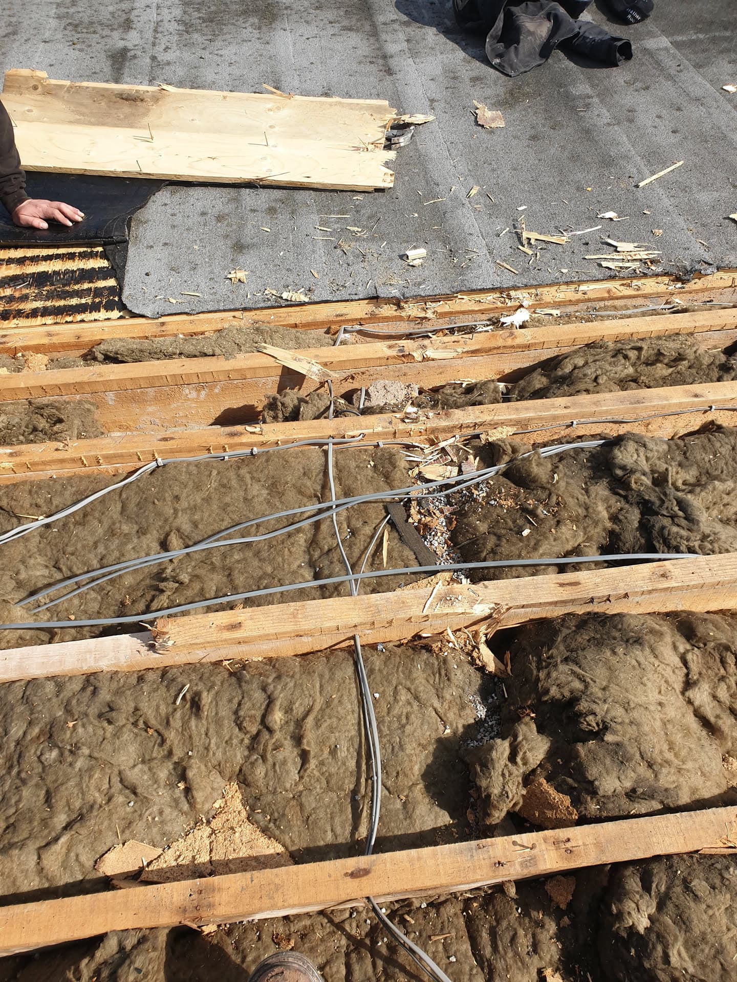 Exposed roof timbers and insulation during flat roof replacement with fitter visible