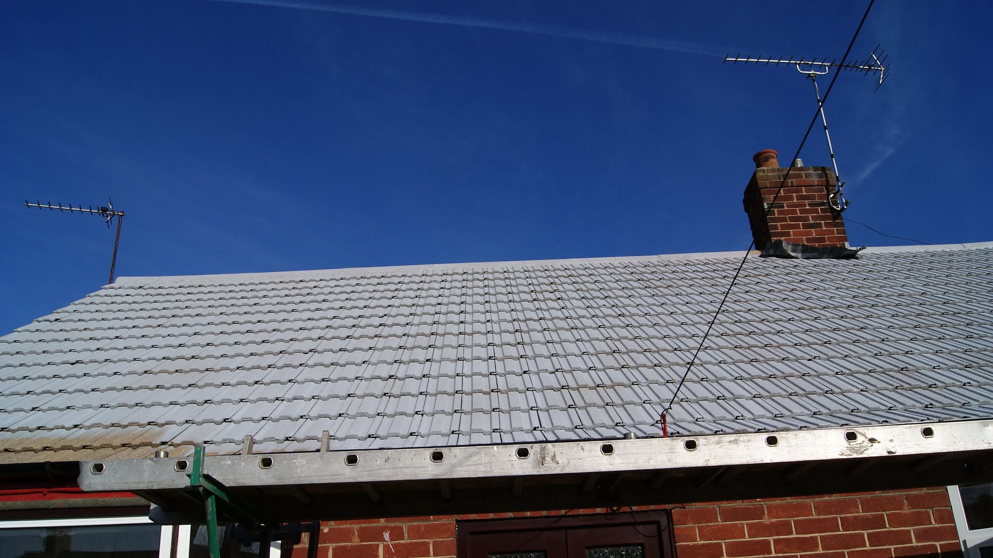 Pitched roof with grey concrete tiles and brick chimney stack with TV aerial