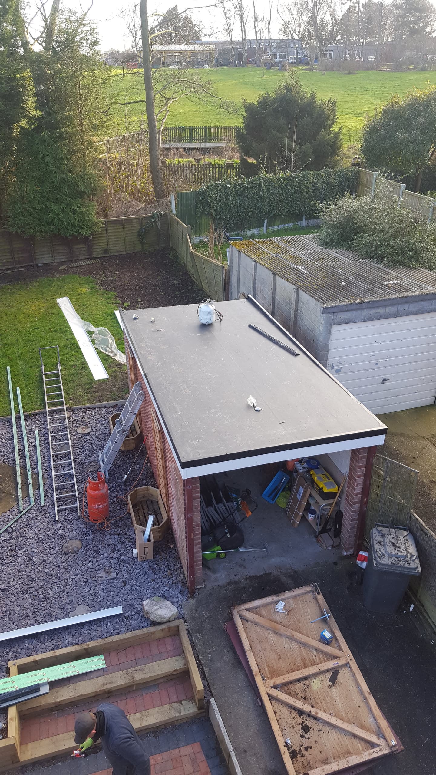 Flat roof installation on brick garage with fitter working on adjacent structure