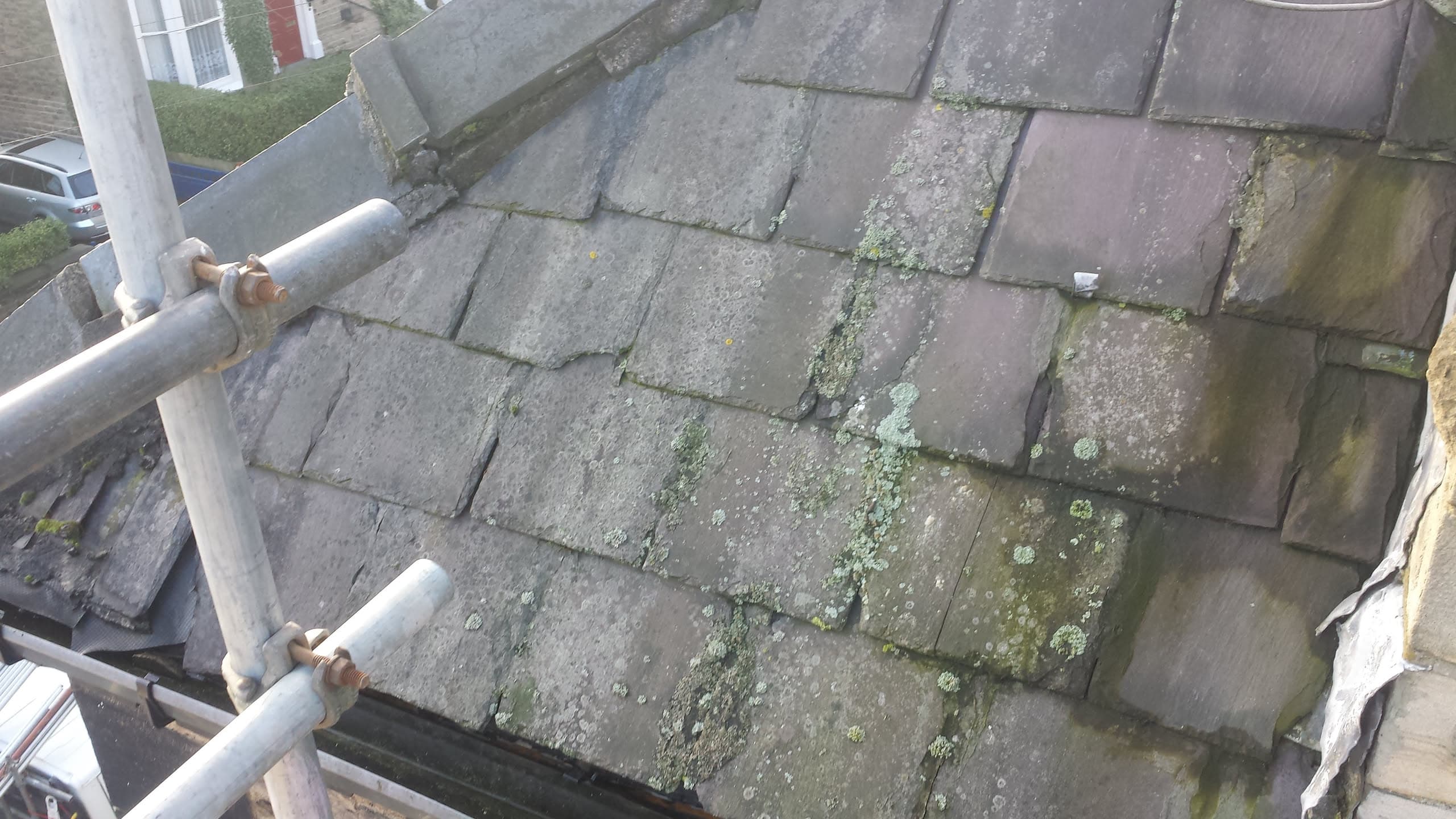 Weathered concrete tiled pitched roof with moss and lichen growth, scaffolding visible