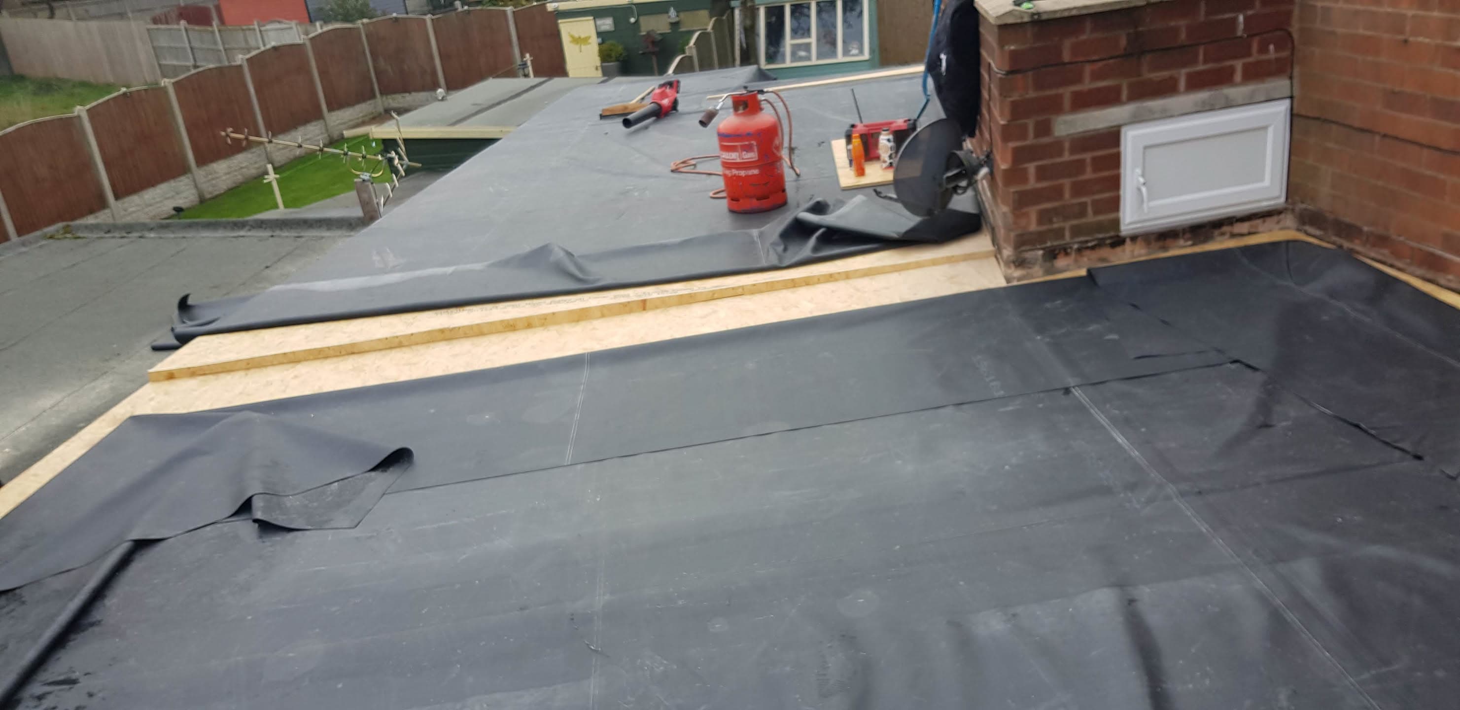 Flat roof installation in progress with grey EPDM rubber membrane and timber edging