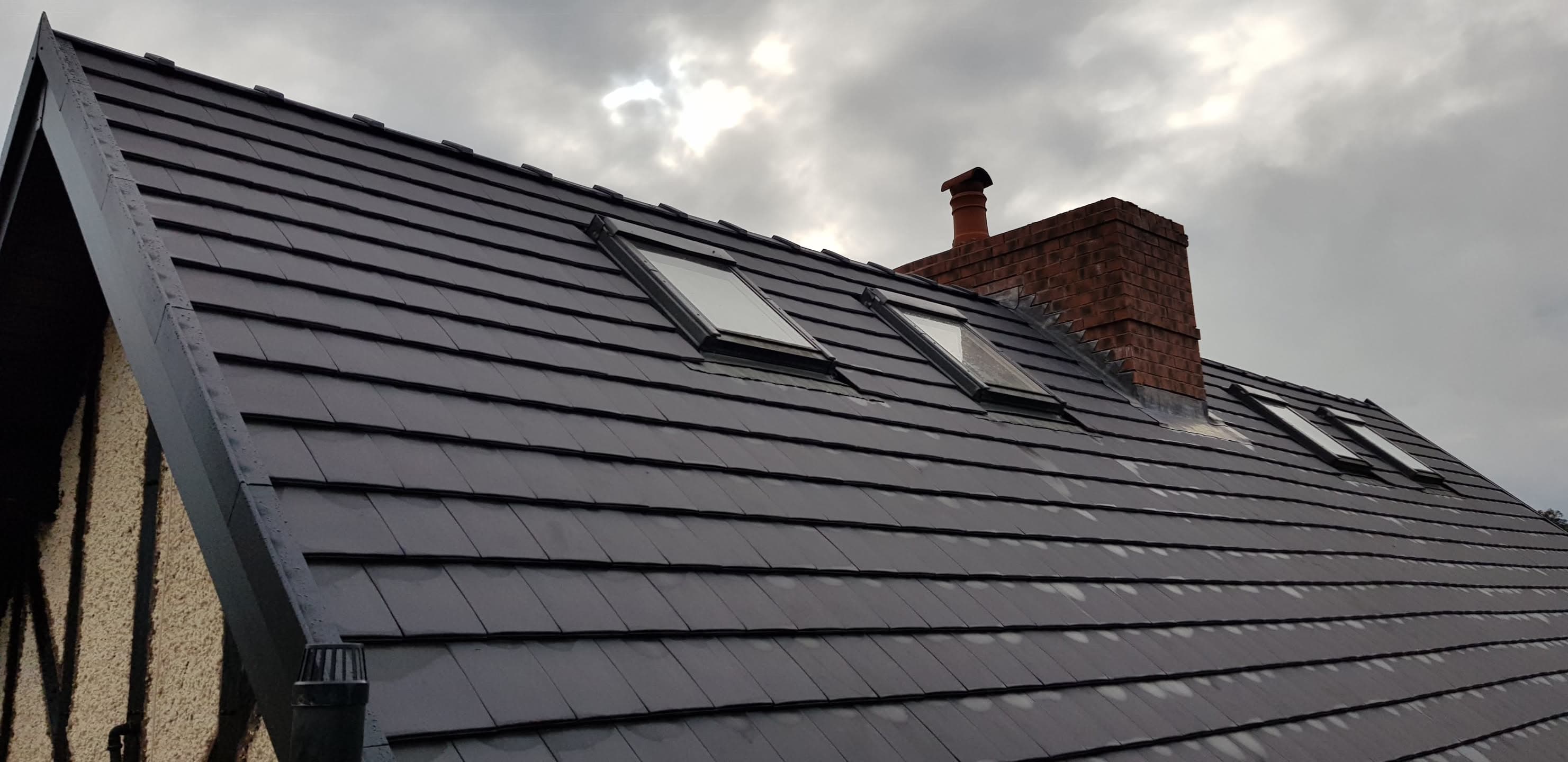 Pitched roof with dark grey slate tiles, two roof windows and red brick chimney stack
