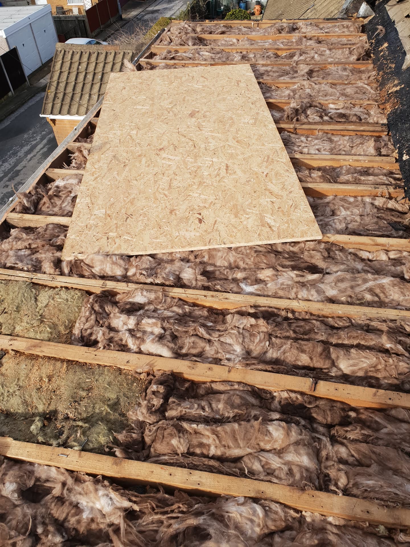 Flat roof installation in progress with exposed timber joists, insulation and OSB boarding