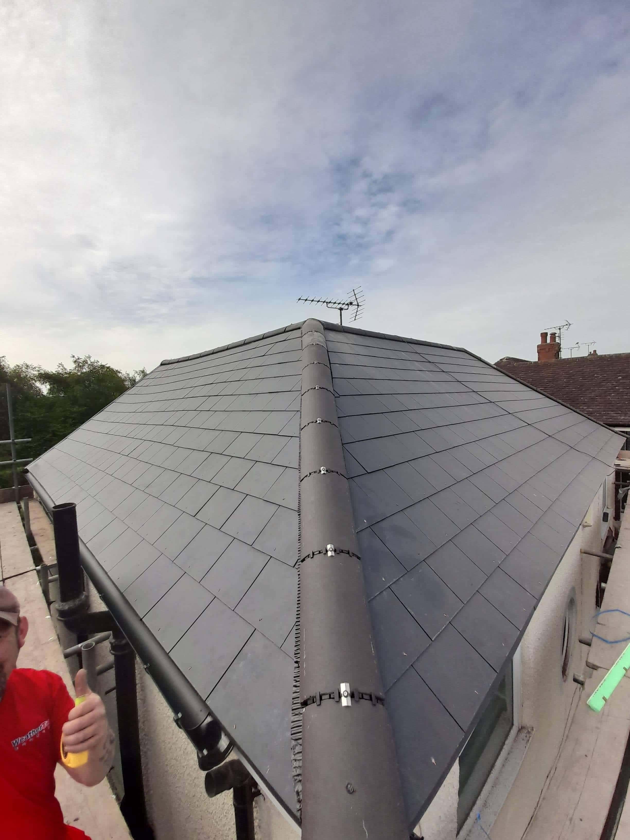 Completed pitched roof with grey slate tiles and dry ridge system, aerial visible at apex