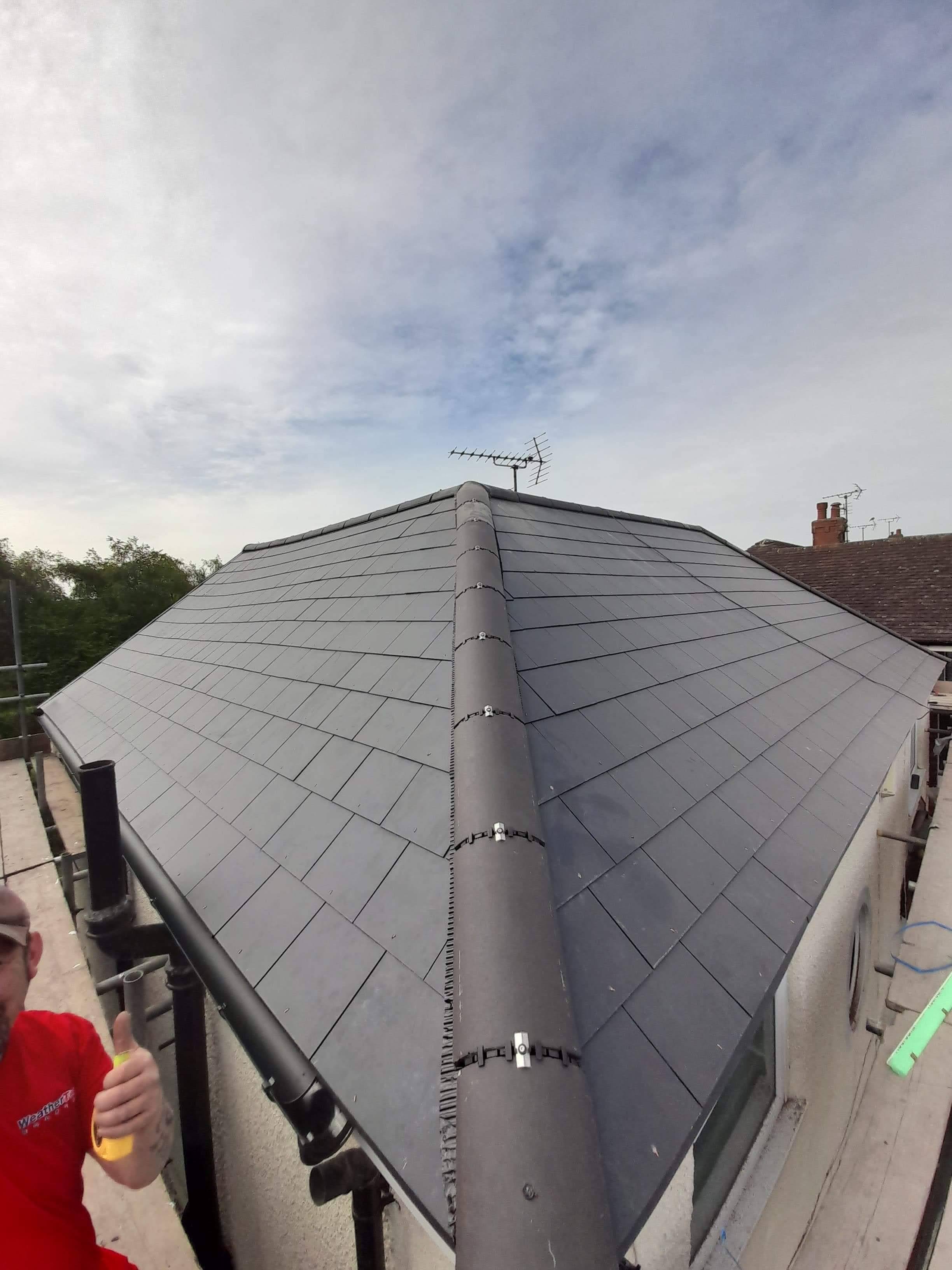 Completed pitched roof with grey slate tiles and dry ridge system, aerial visible at apex