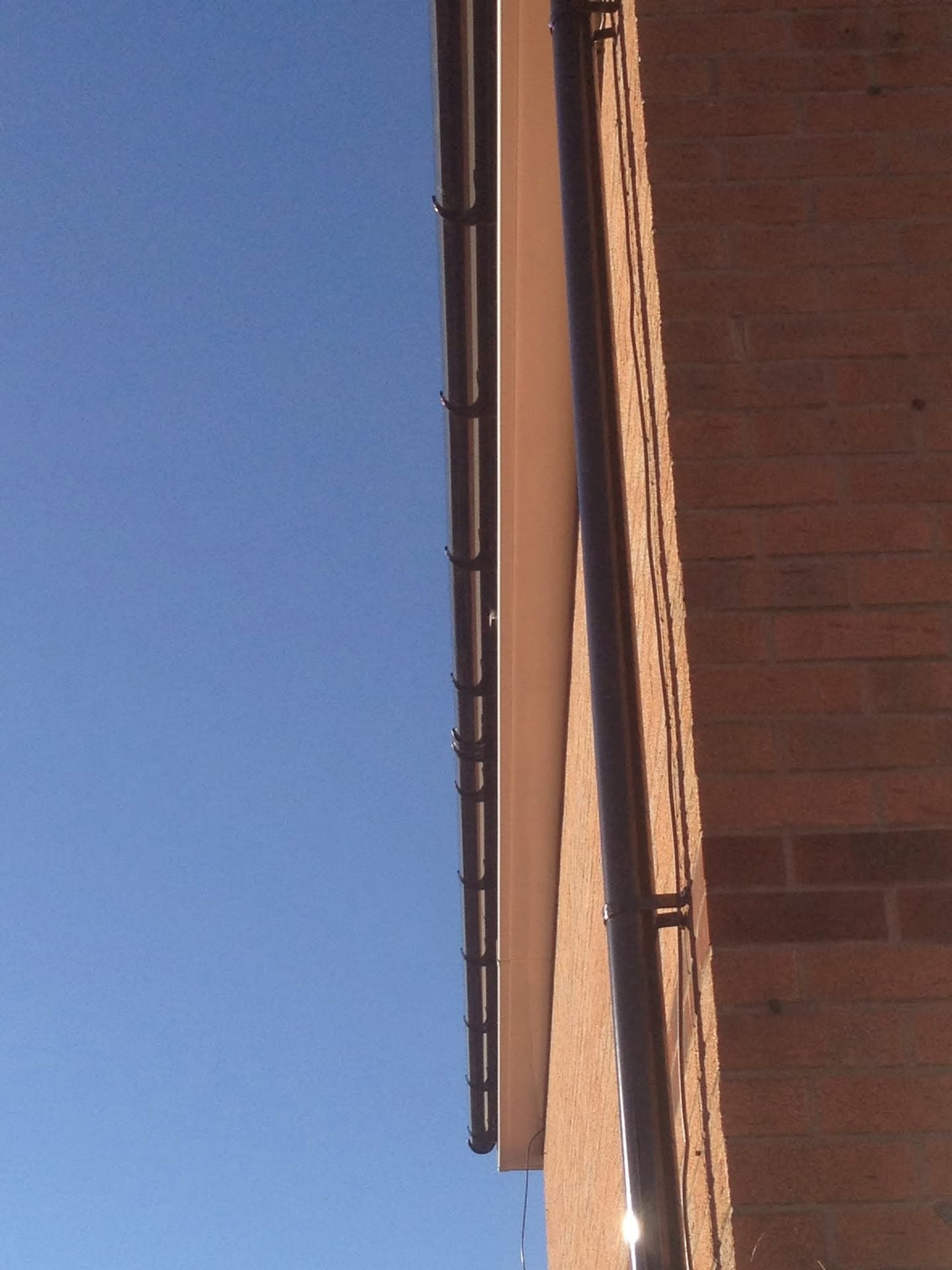 Brown fascia board and guttering installed on brick building against clear blue sky