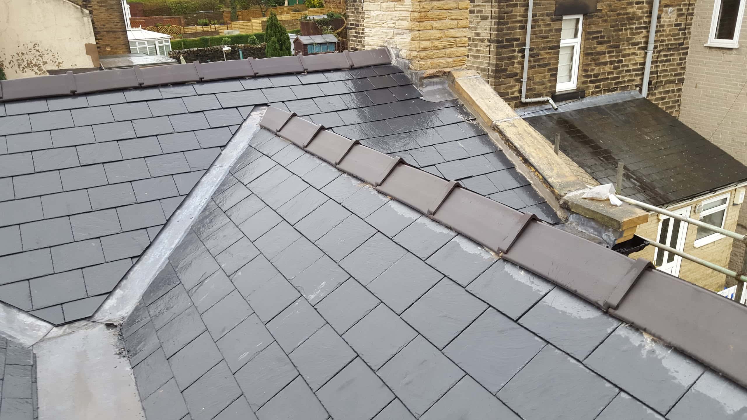 Newly completed grey slate pitched roof with ridge tiles and lead flashing