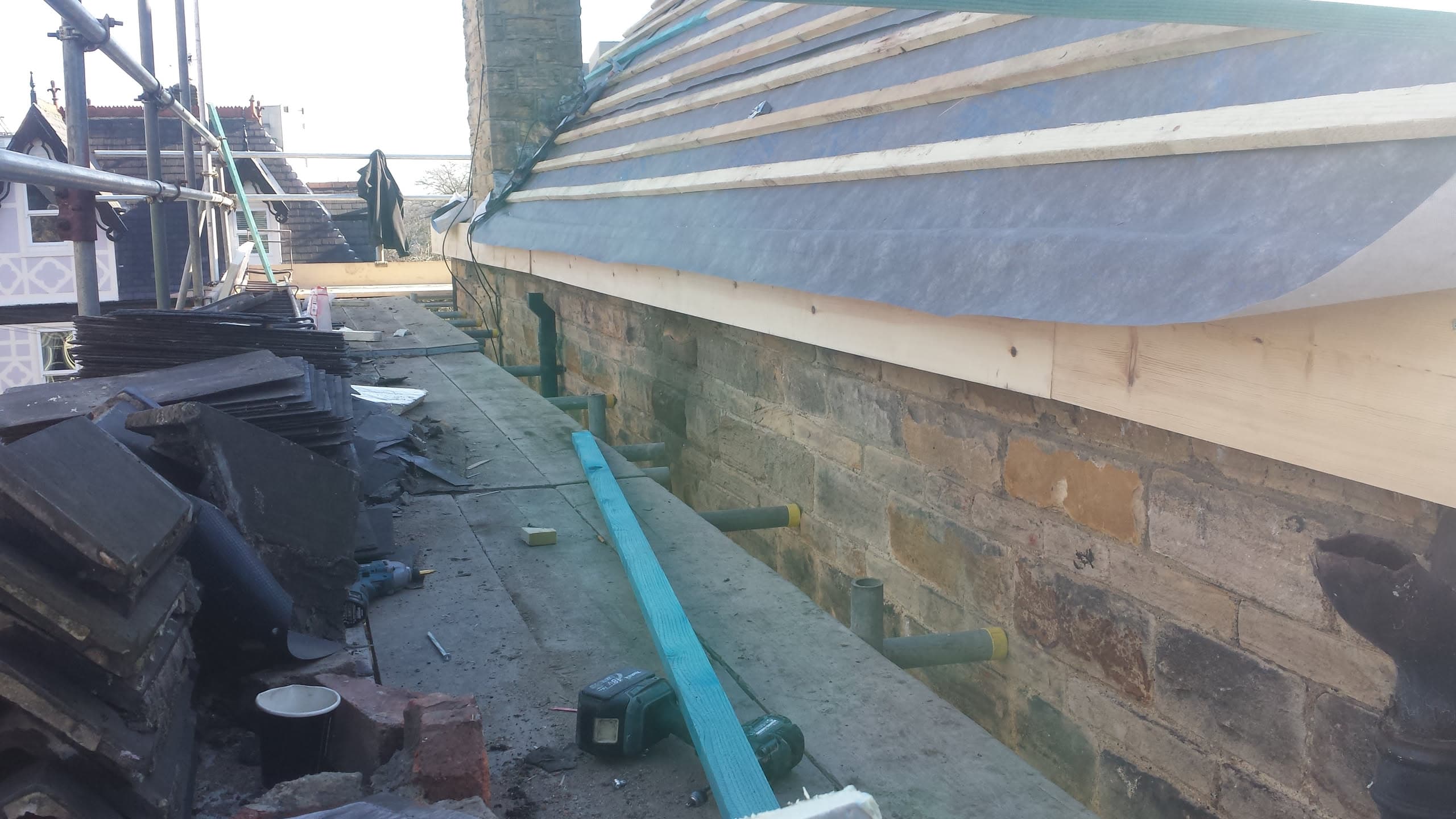 Flat roof installation in progress with timber battens and felt membrane around brick chimney
