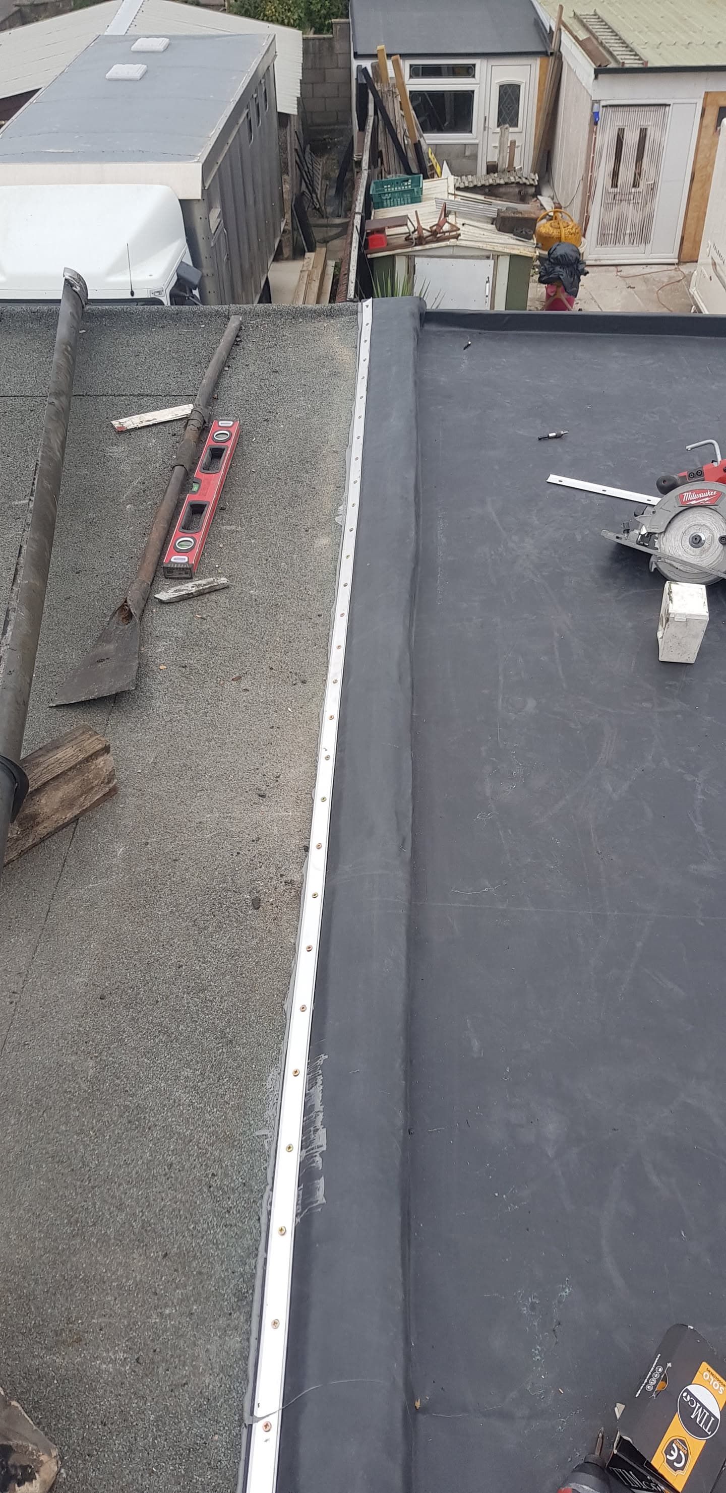 Flat roof installation in progress with dark grey felt and metal trim edging