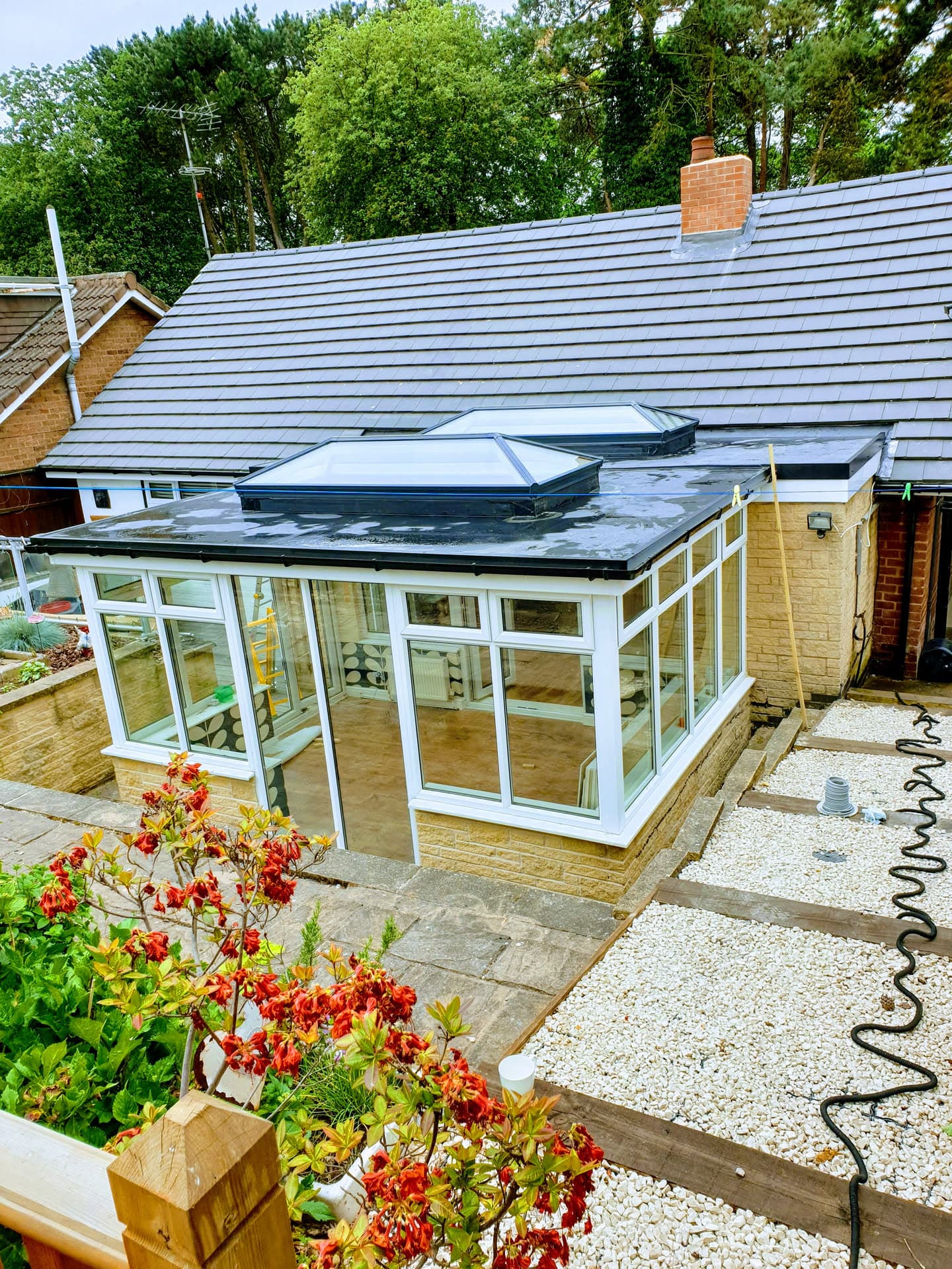 Grey tiled pitched roof with flat conservatory roof featuring anthracite rooflights and brick chimney