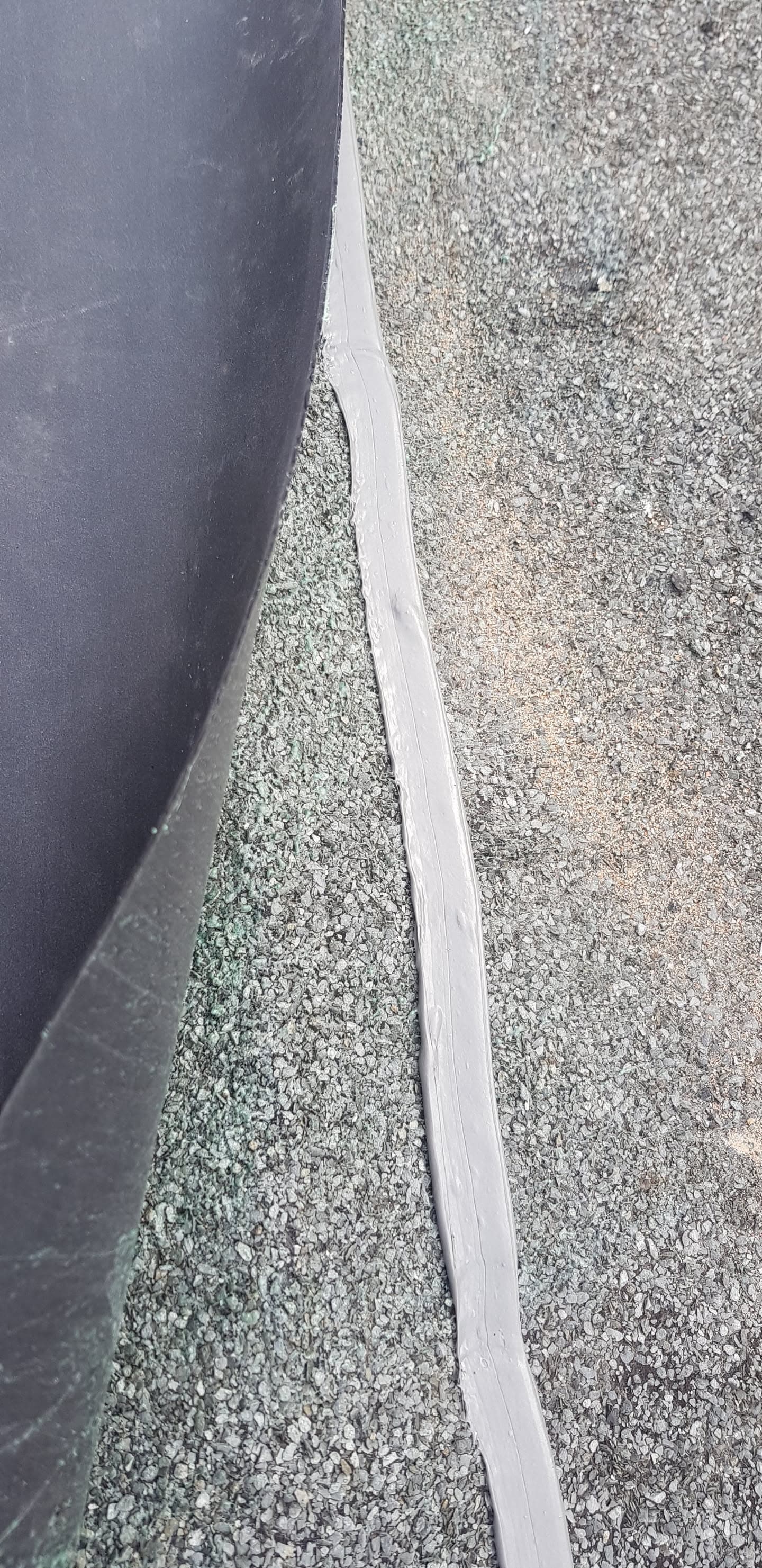 Close-up detail of grey felt flat roof edge trim and mineral chippings